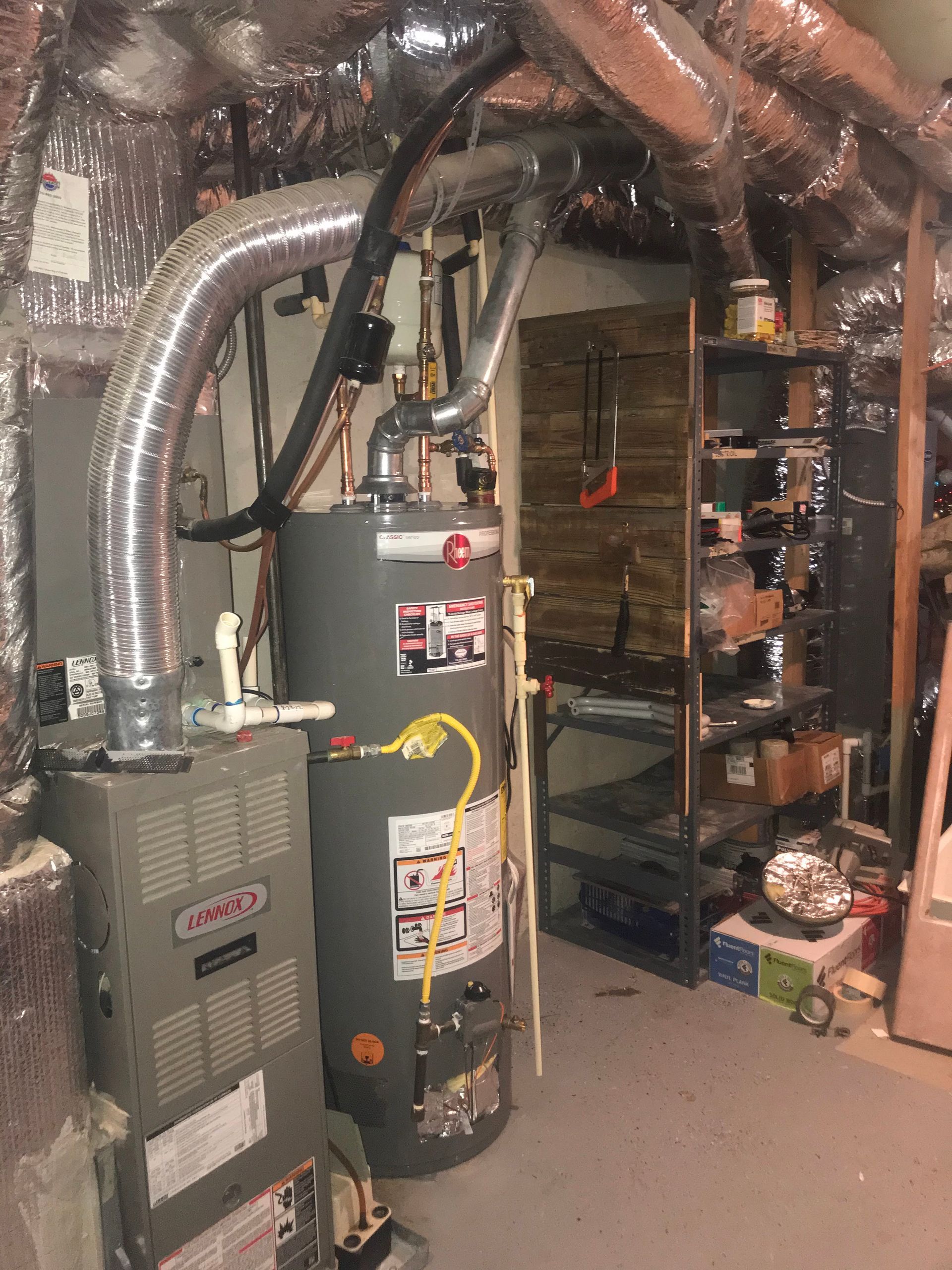 Furnace and water heater in a utility room with metal ductwork and storage shelves.