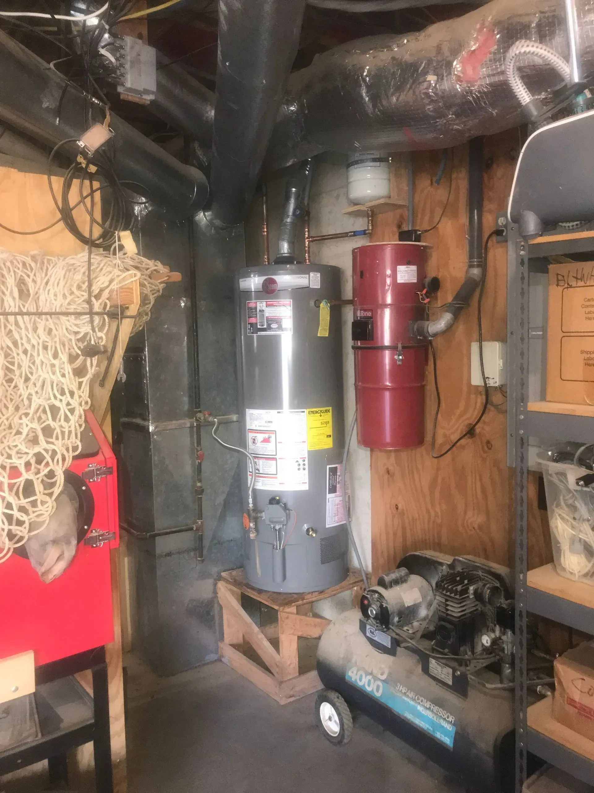 Water heater and air compressor in a basement setting, with ductwork and central vacuum unit.