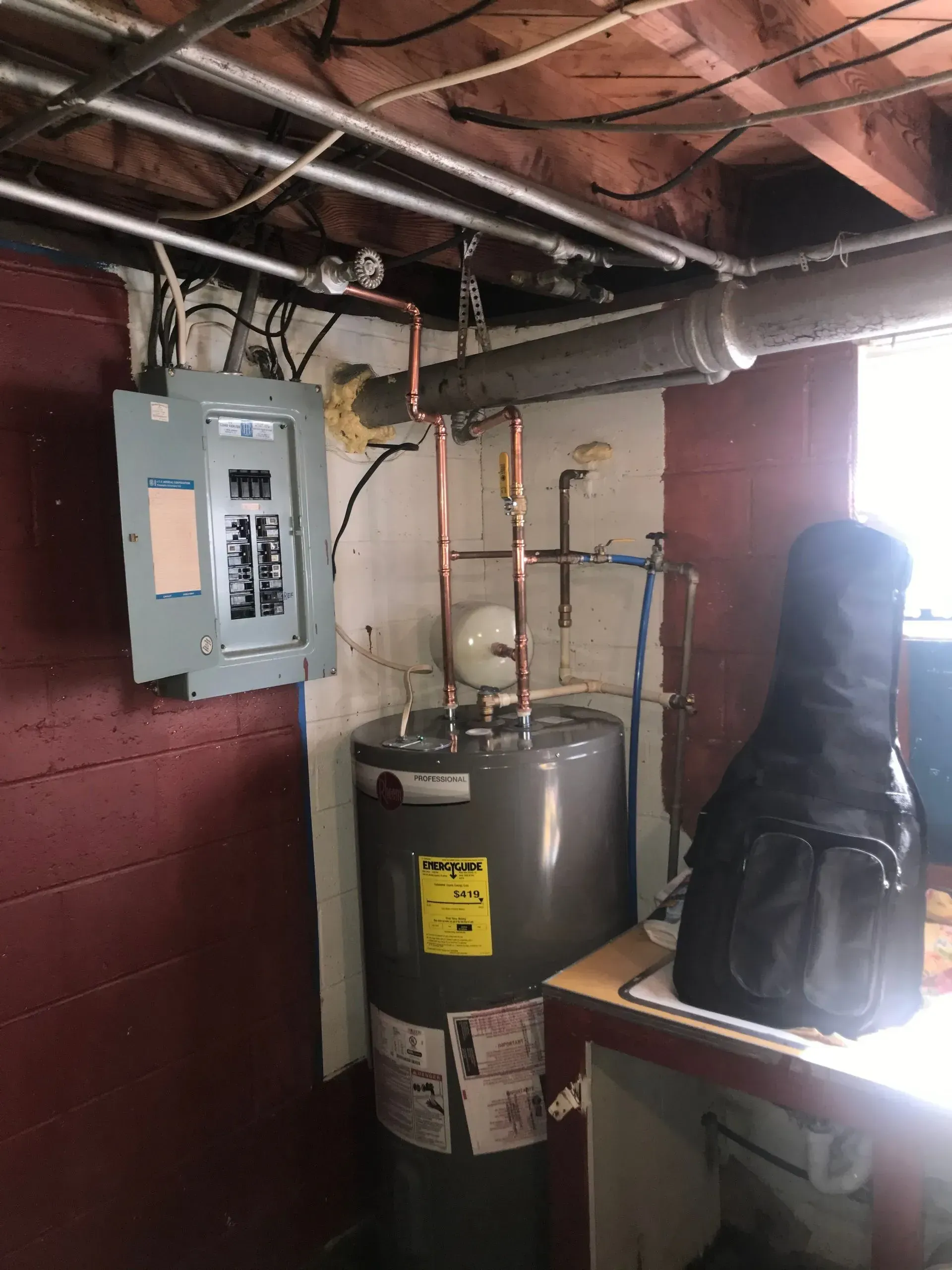 Electrical panel, water heater, and guitar case in a basement corner.