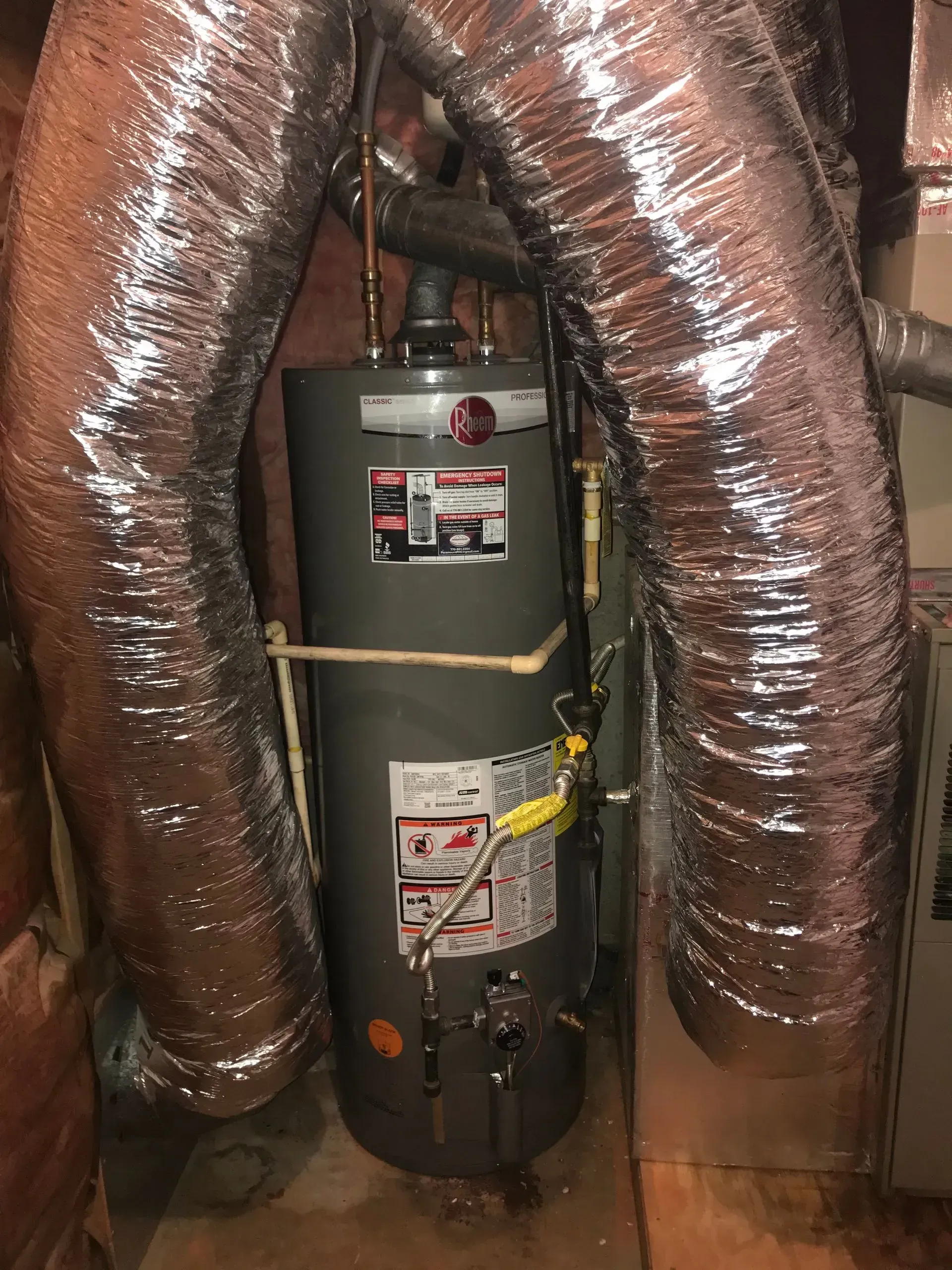 A tall, gray water heater with two silver duct tubes in a room.