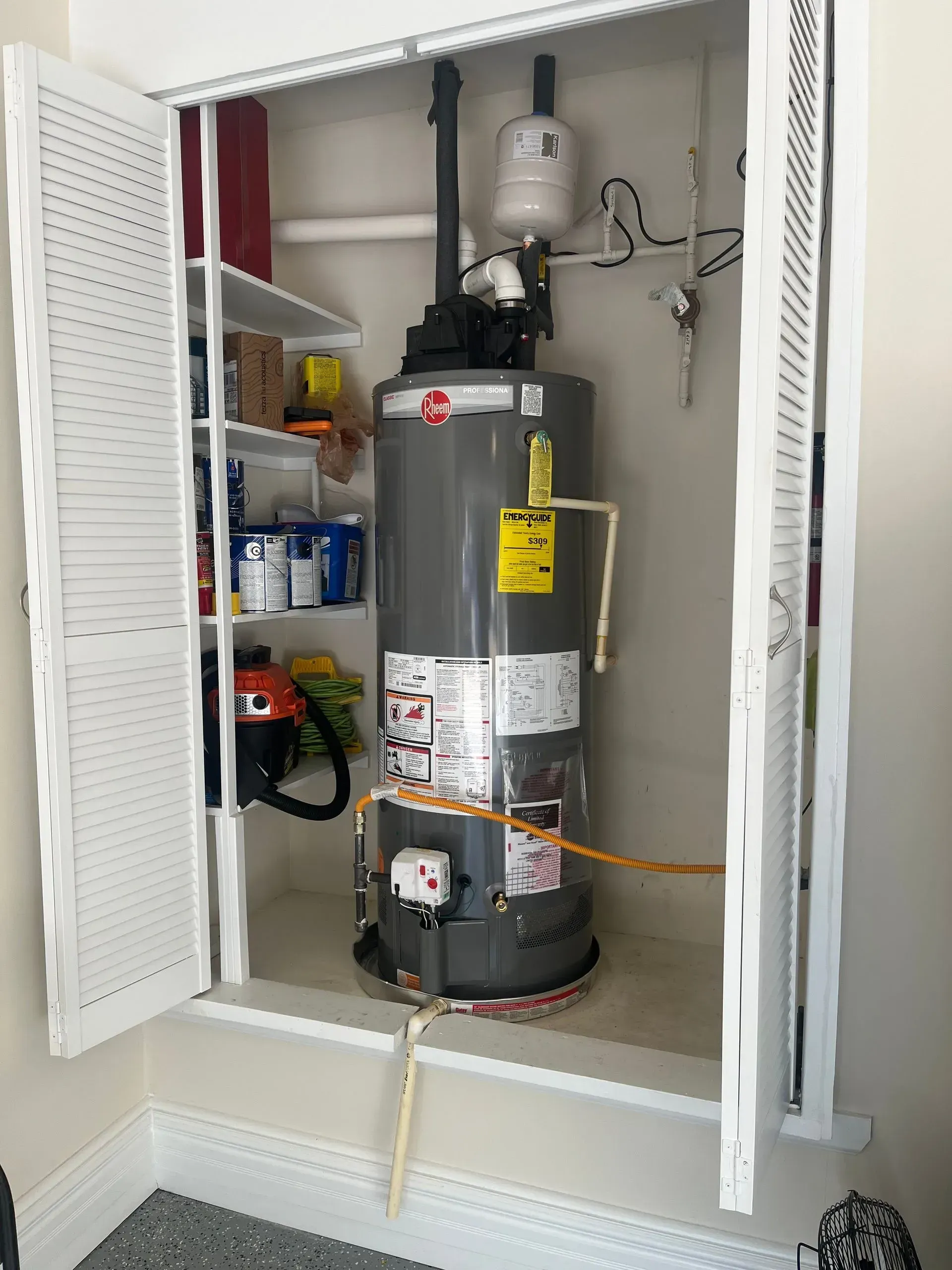 A closet containing a Rheem water heater, shelves with supplies, and open white louvered doors.