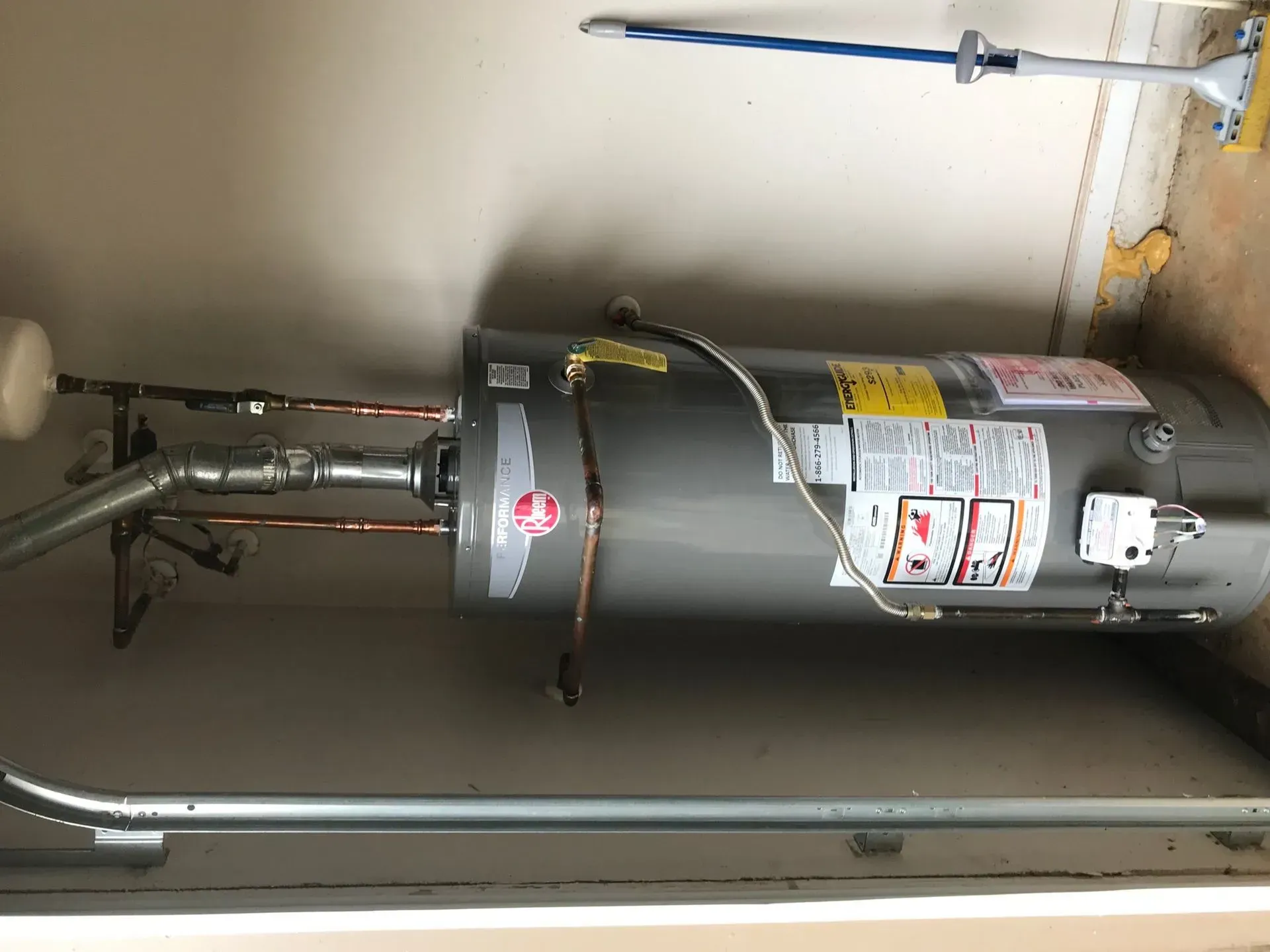 A Rheem water heater installed in a garage with copper pipes and a pressure relief valve.