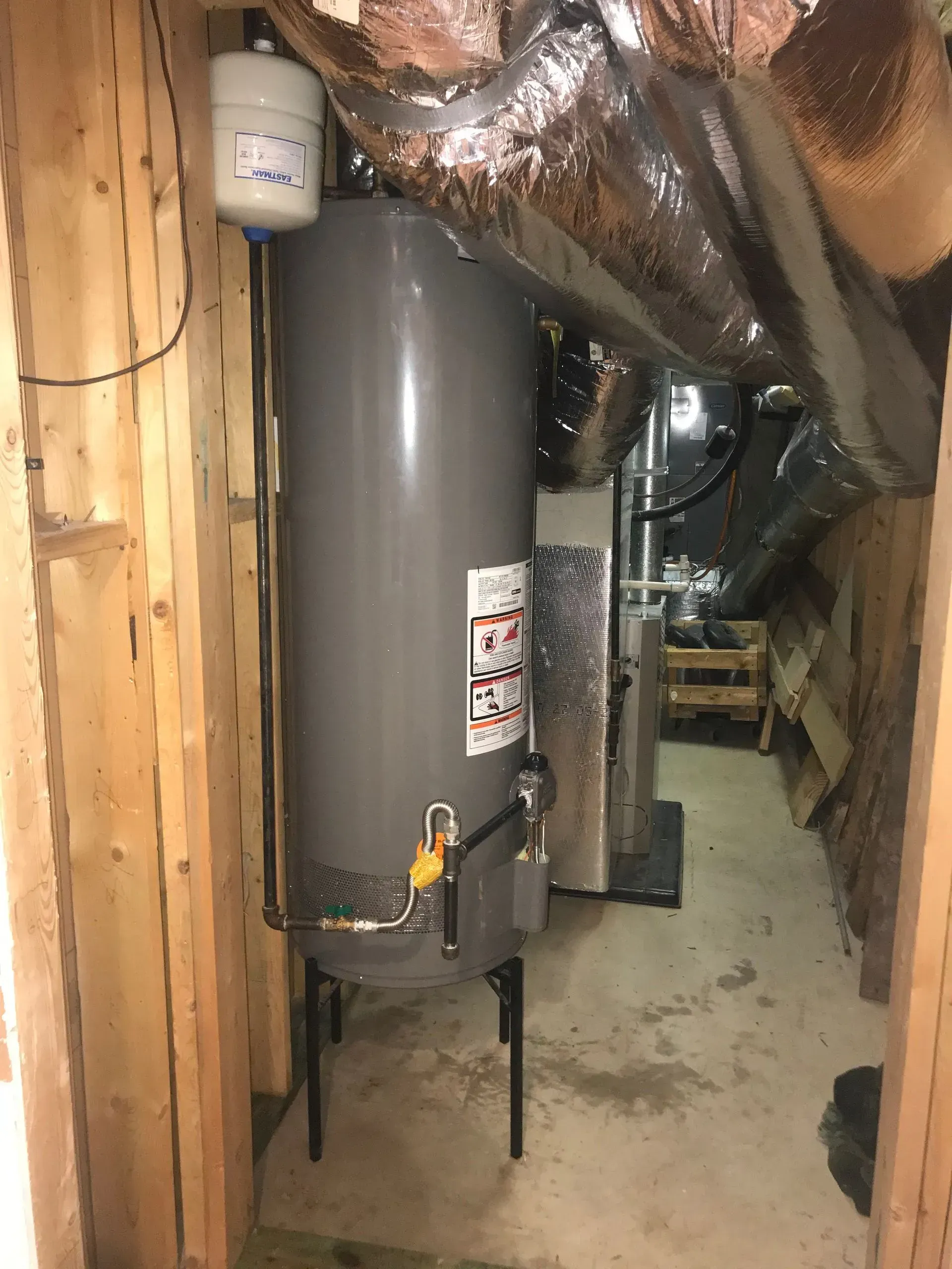 Gray water heater in a narrow, unfinished basement room.