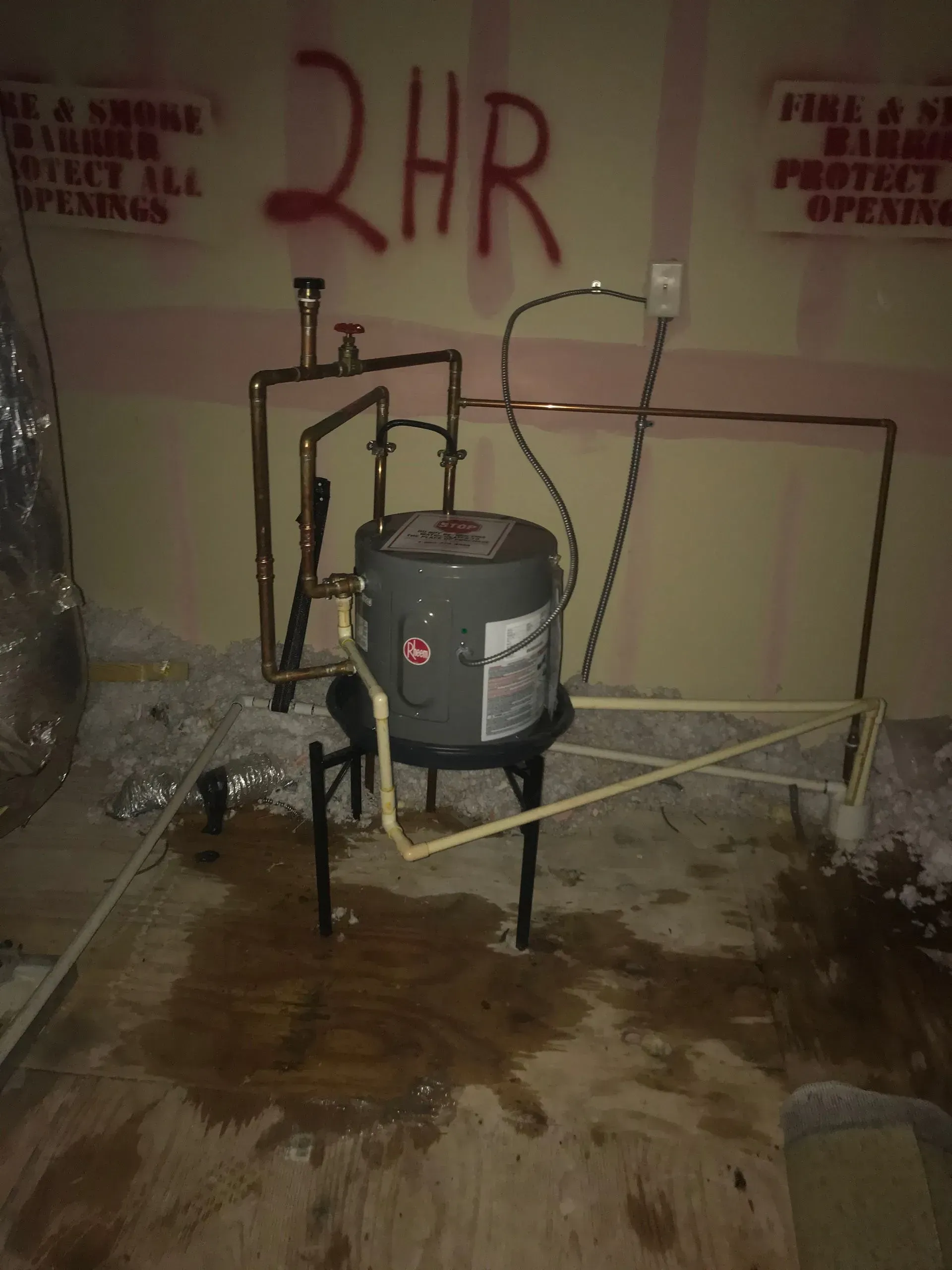 Water heater on stand, copper pipes, electrical wiring, and water on floor in a utility room.