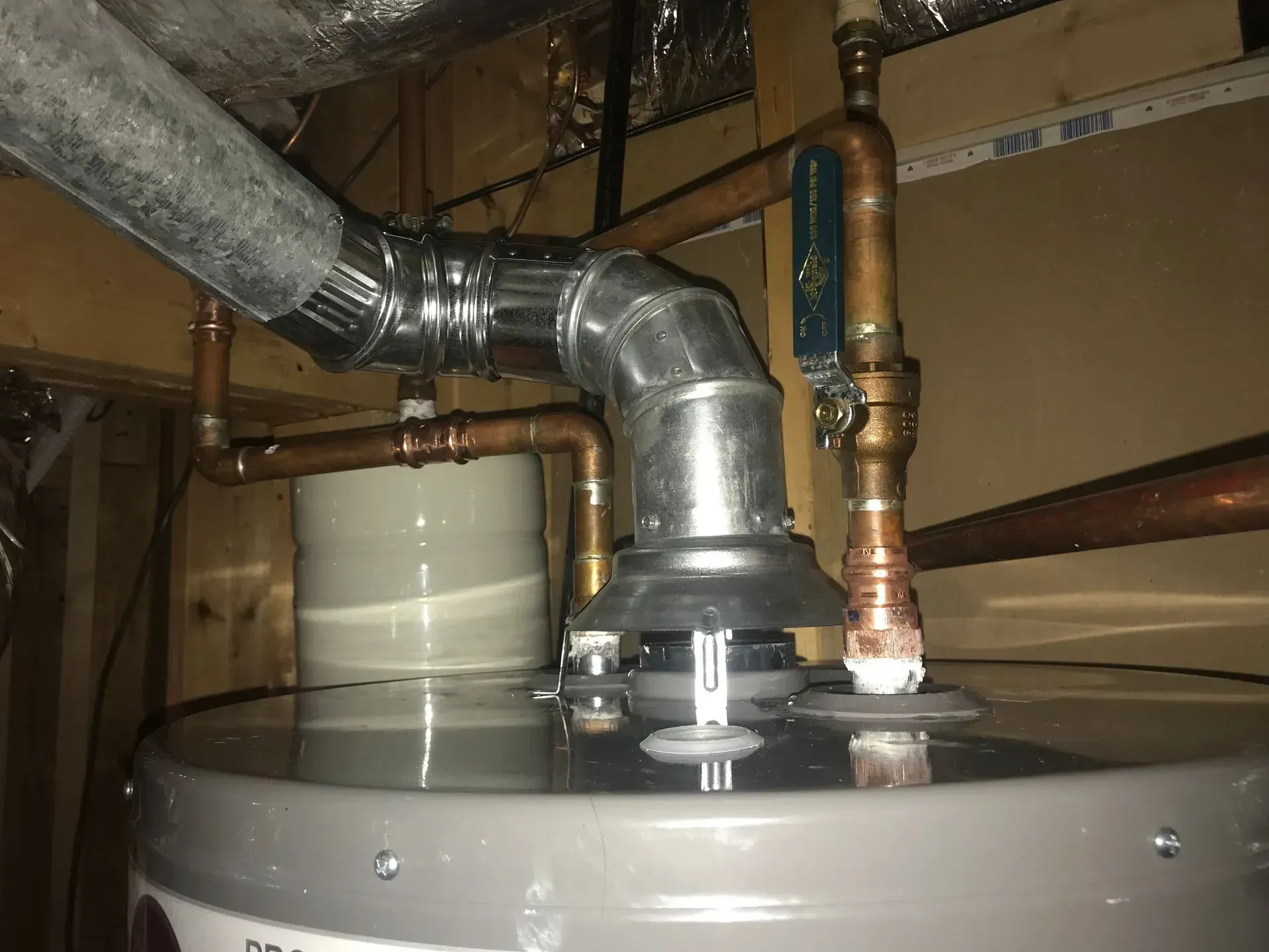 A water heater with silver metal exhaust pipe connected to it, located in a basement.