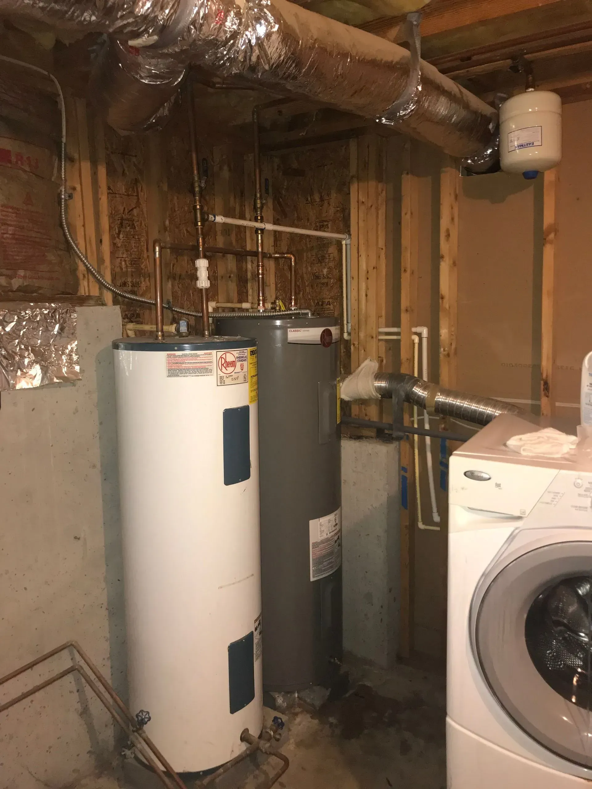 Two water heaters and a washing machine in a basement. Plumbing pipes visible.