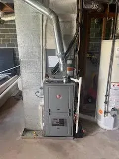 Furnace and water heater in a basement. Gray furnace with metal exhaust pipe. White water heater.