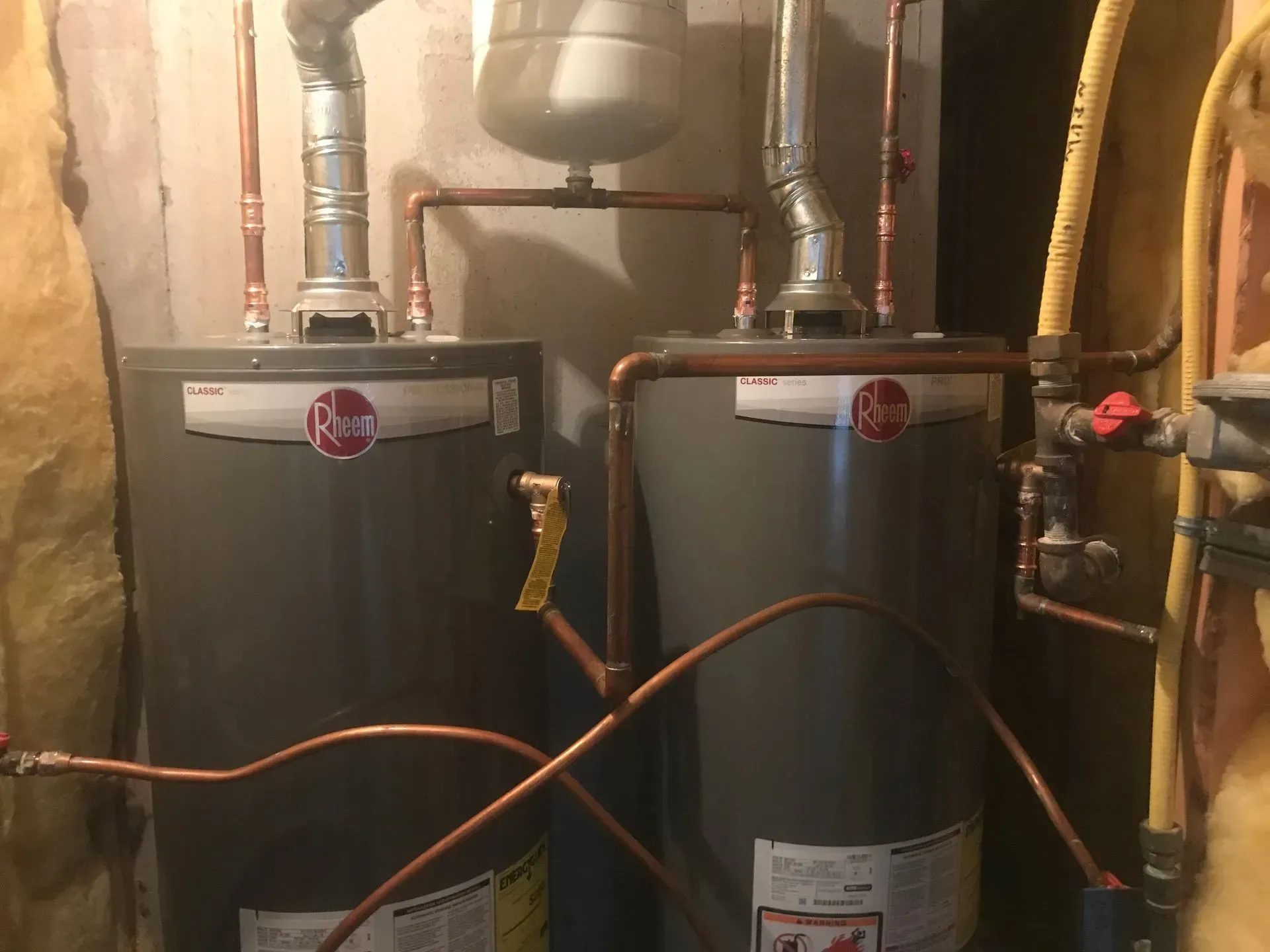 Two gray Rheem water heaters with copper pipes in a basement.