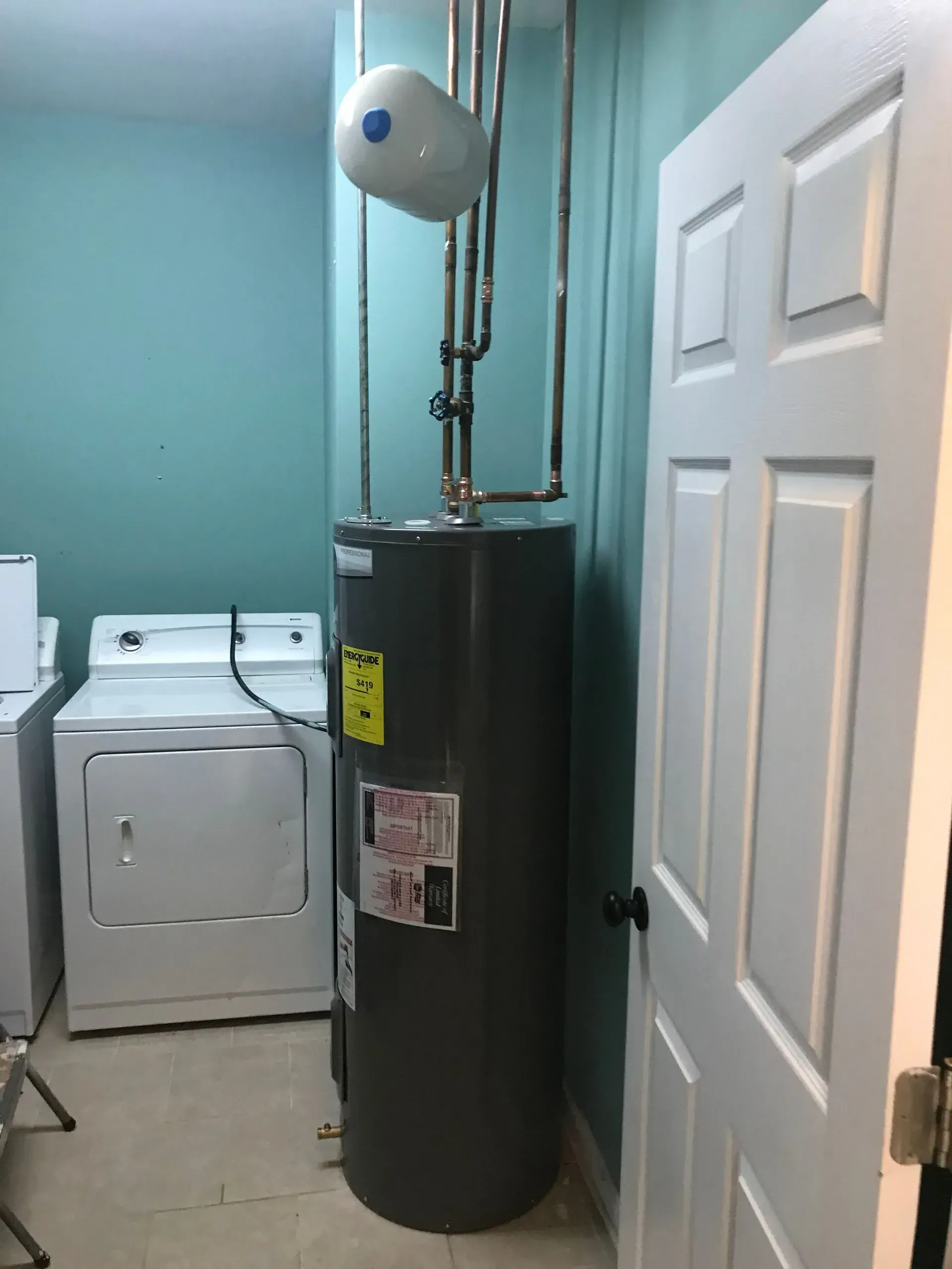 A water heater and laundry machines in a laundry room with teal walls and a white door.