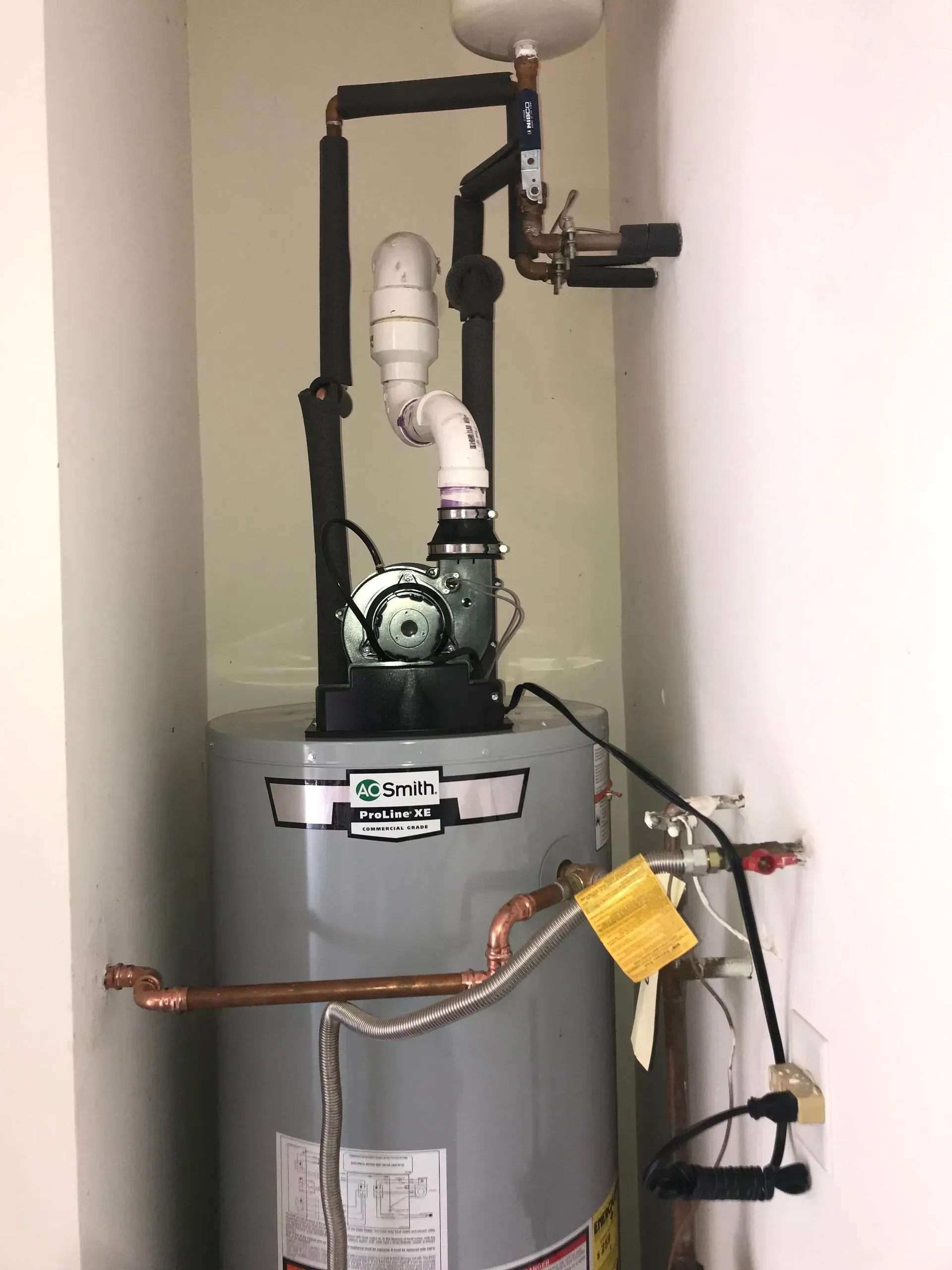 Water heater in a corner, pipes and pump attached.