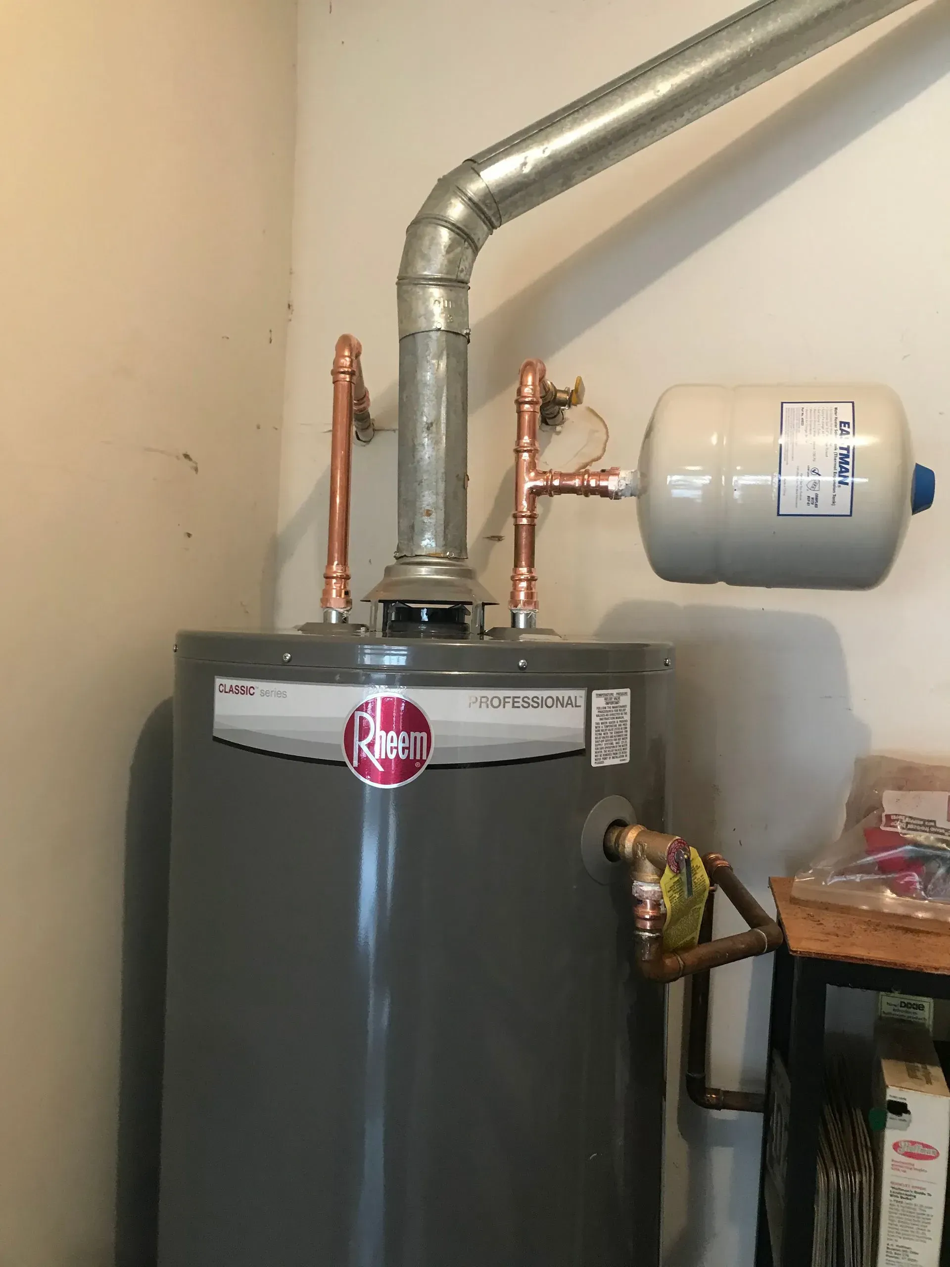 A water heater with copper pipes and a silver expansion tank, in a utility room.