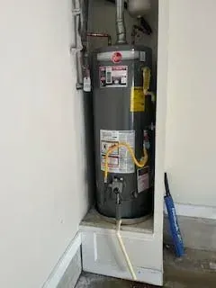 Gray water heater in a recessed alcove, with pipes and yellow gas line.