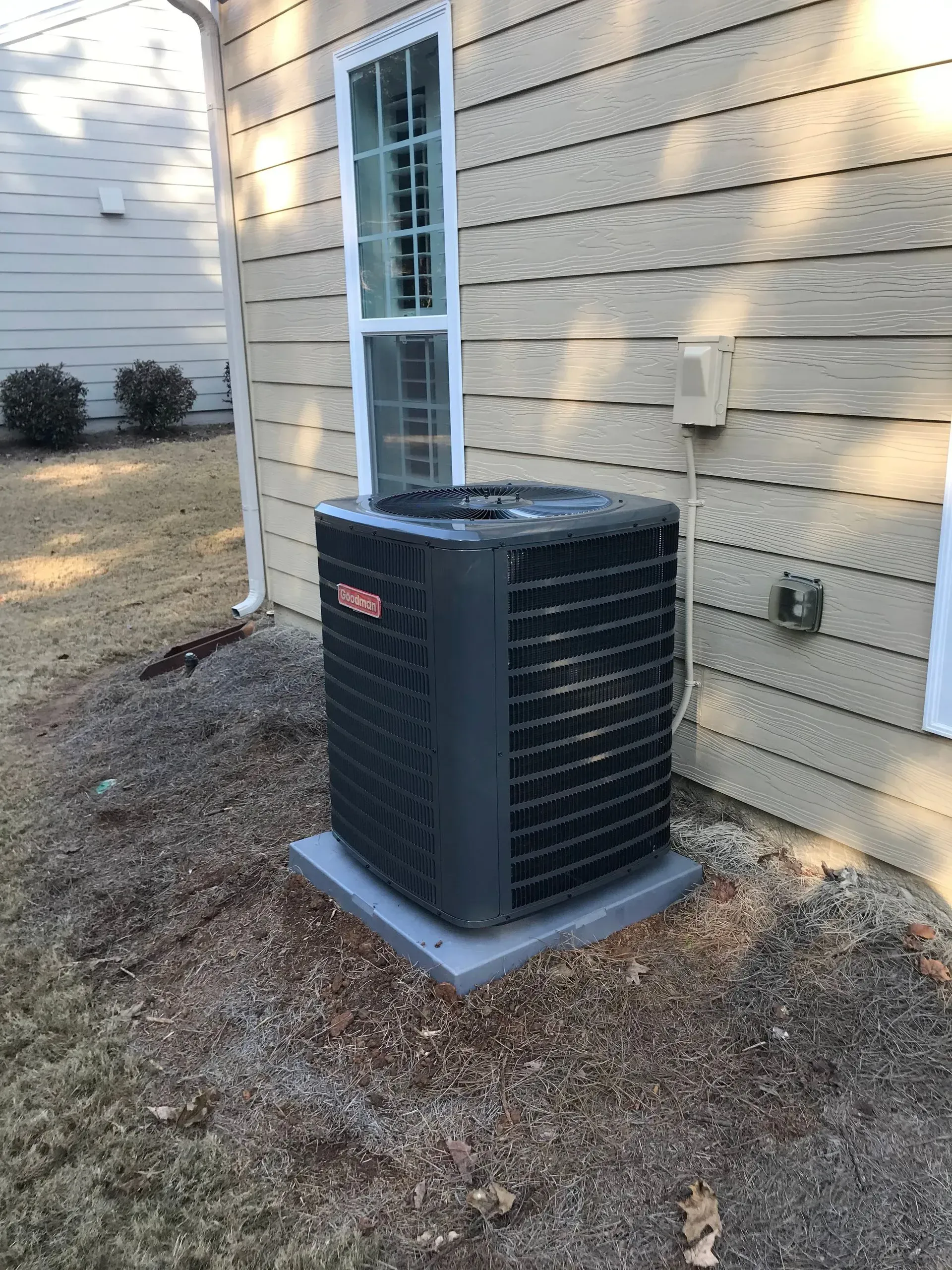 HVAC unit on a concrete pad outside a house with beige siding and a window.