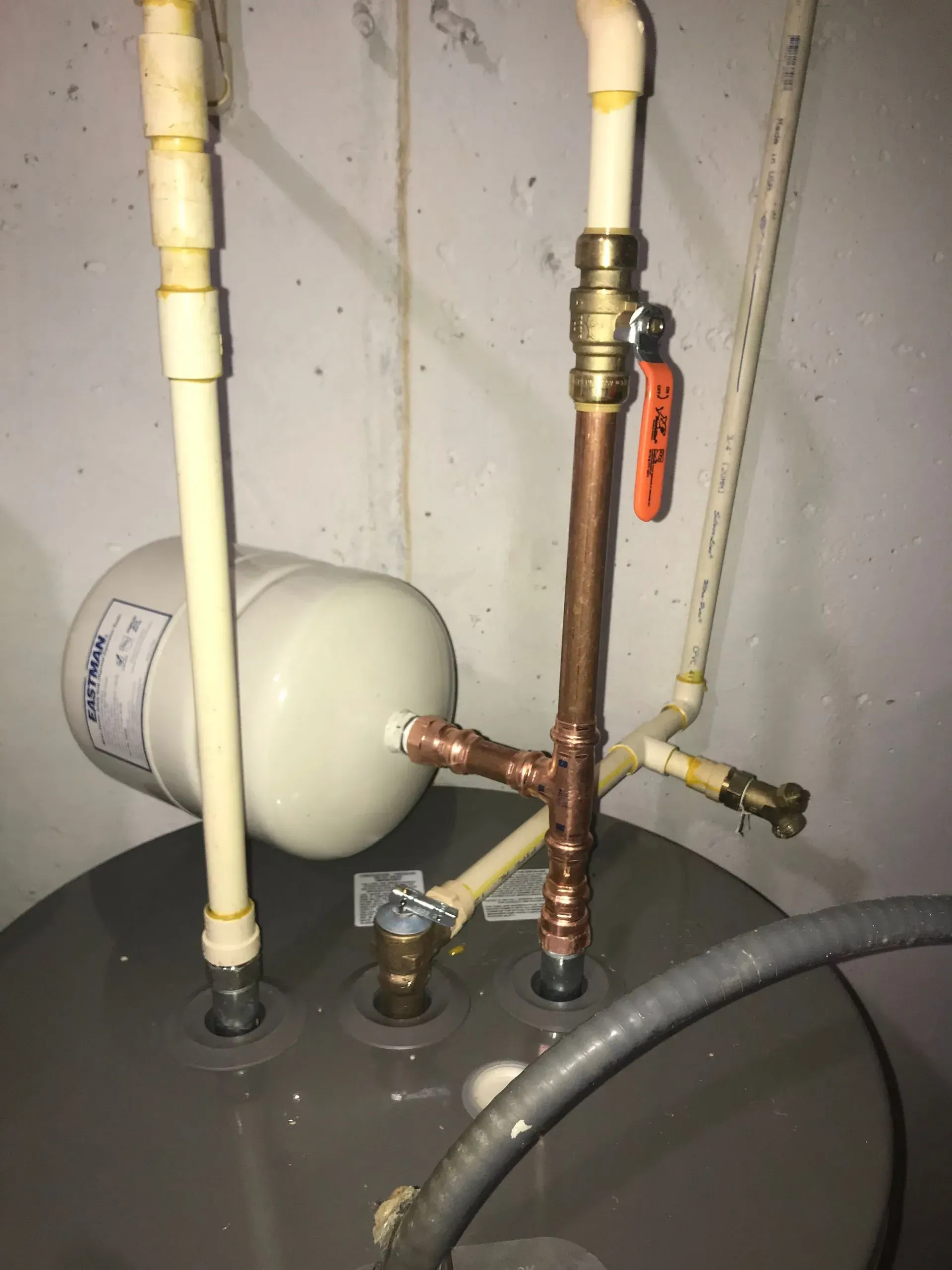 Plumbing with pipes and a water tank. Copper and plastic pipes, shut off valve, expansion tank, in a basement.