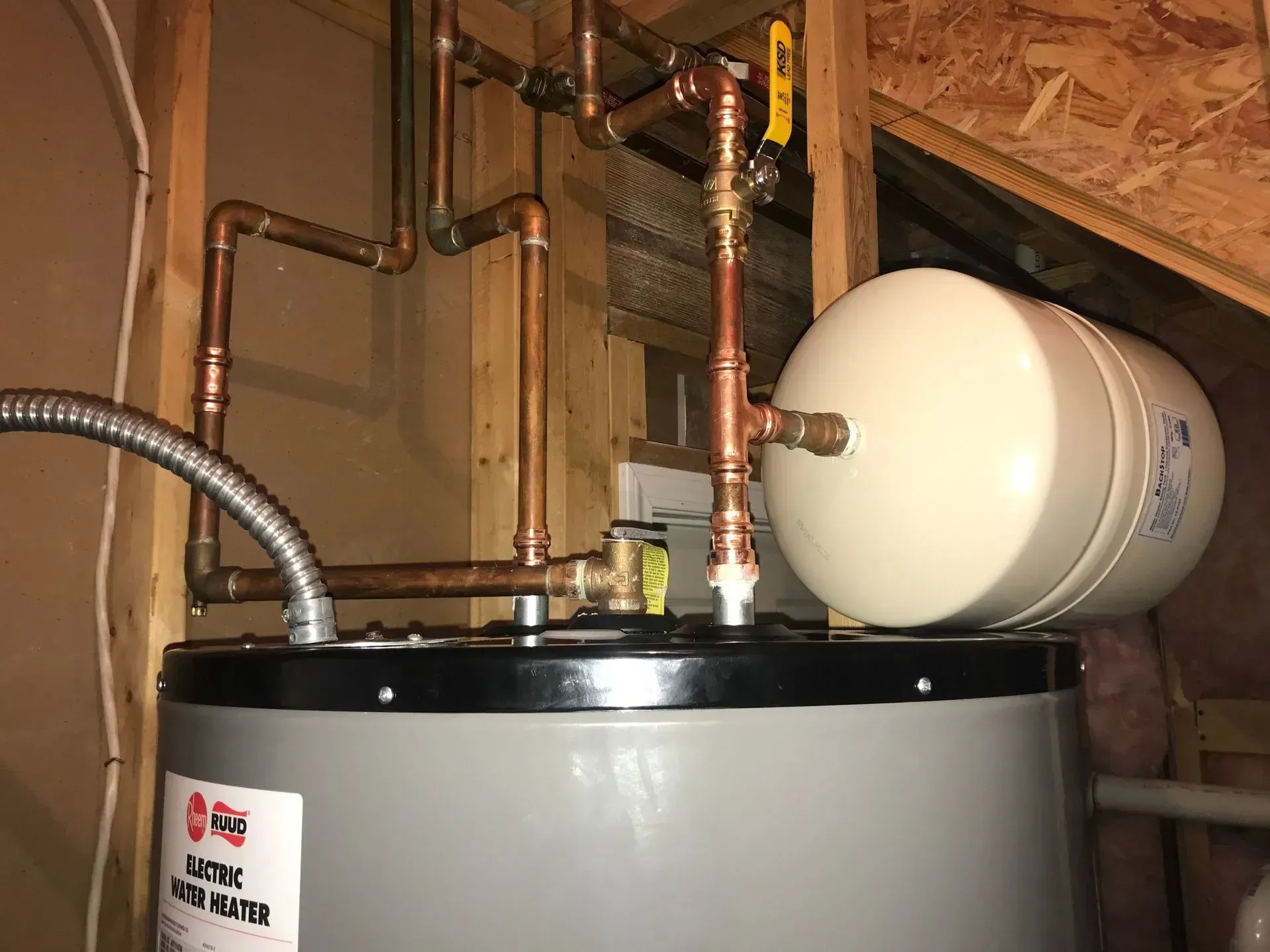 Water heater with copper pipes and a white expansion tank in a utility room.