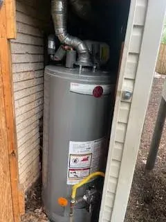 Gray water heater in a shed, with a metal flue, and yellow gas line.