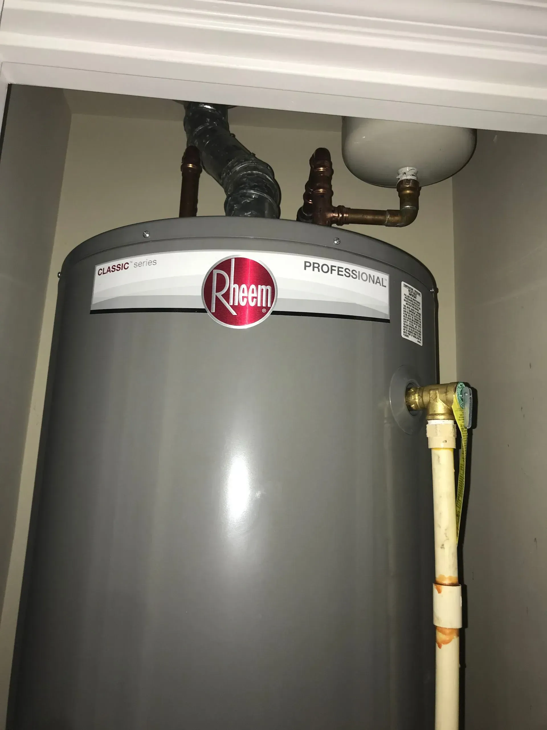 Gray Rheem water heater in a small closet with white walls.