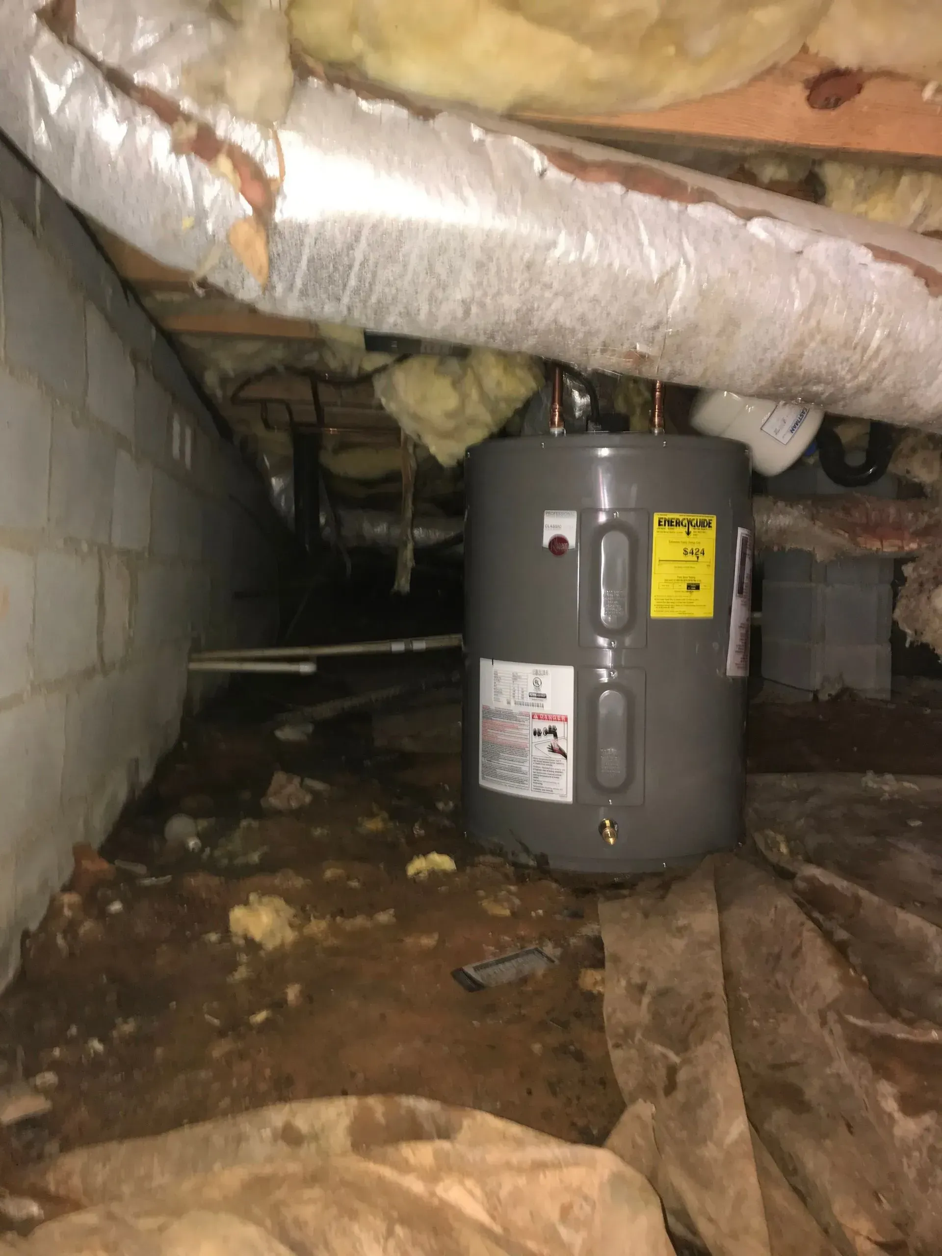 Water heater in crawl space, surrounded by insulation, ductwork, and uneven ground.