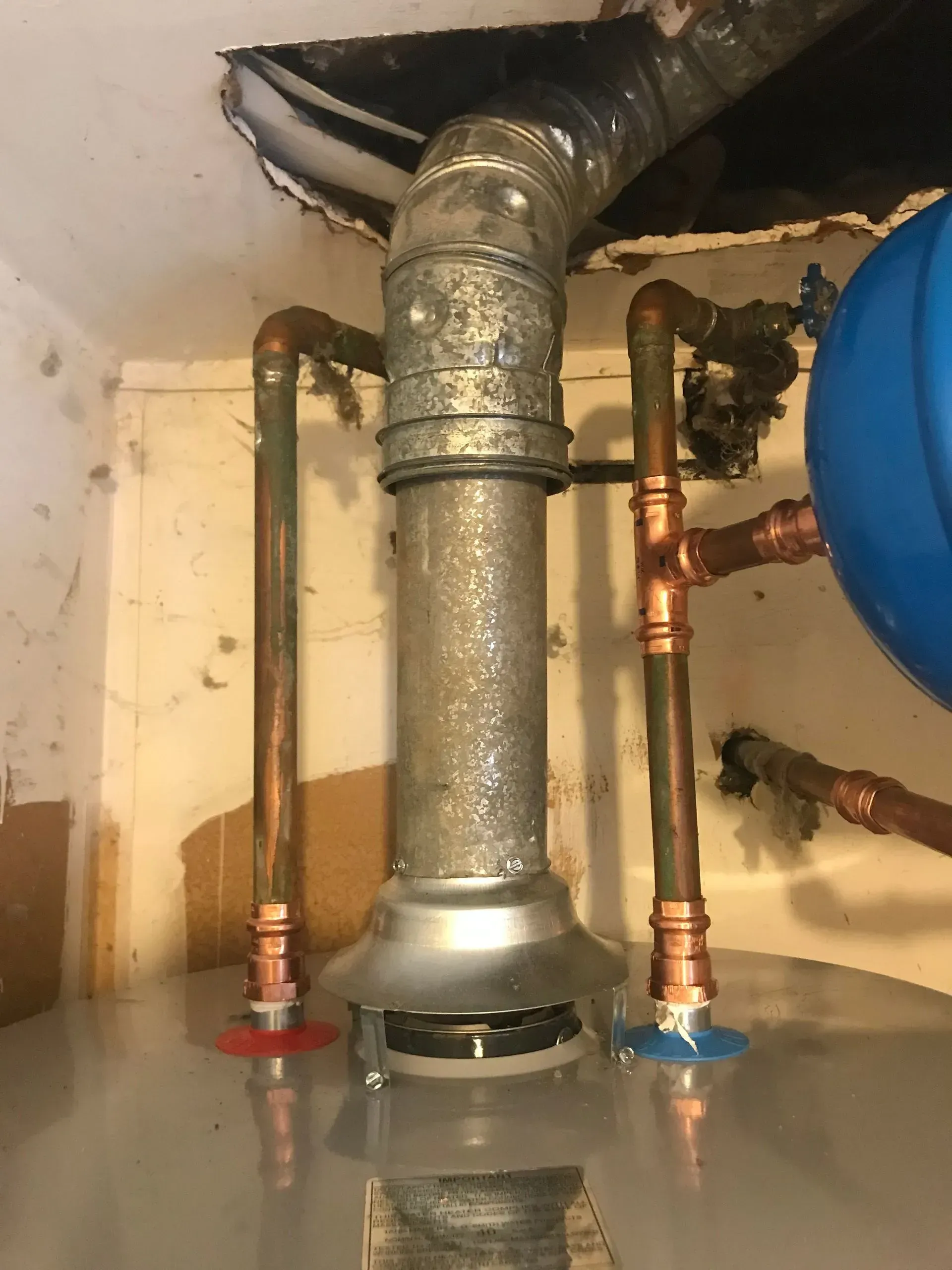 A water heater with copper pipes and vent. The pipes connect to the ceiling.