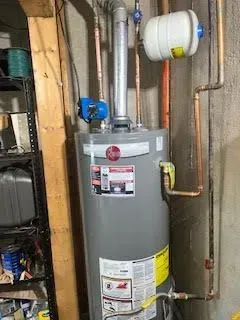 A gray Rheem water heater with copper pipes in a basement. Blue and white components are attached.
