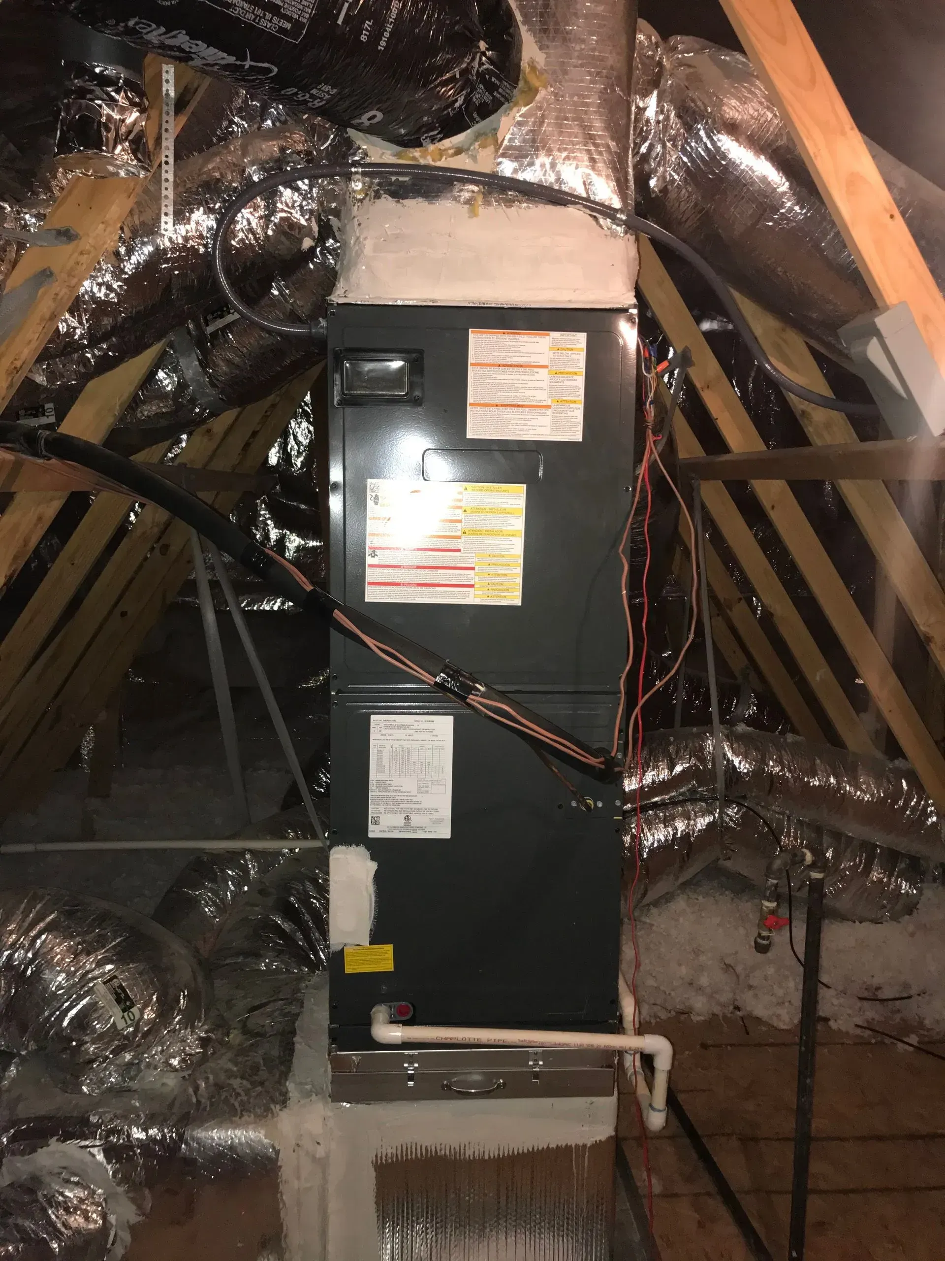An HVAC system in an attic, surrounded by insulation and wooden beams.