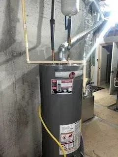 Gray water heater with pipes in a basement setting.