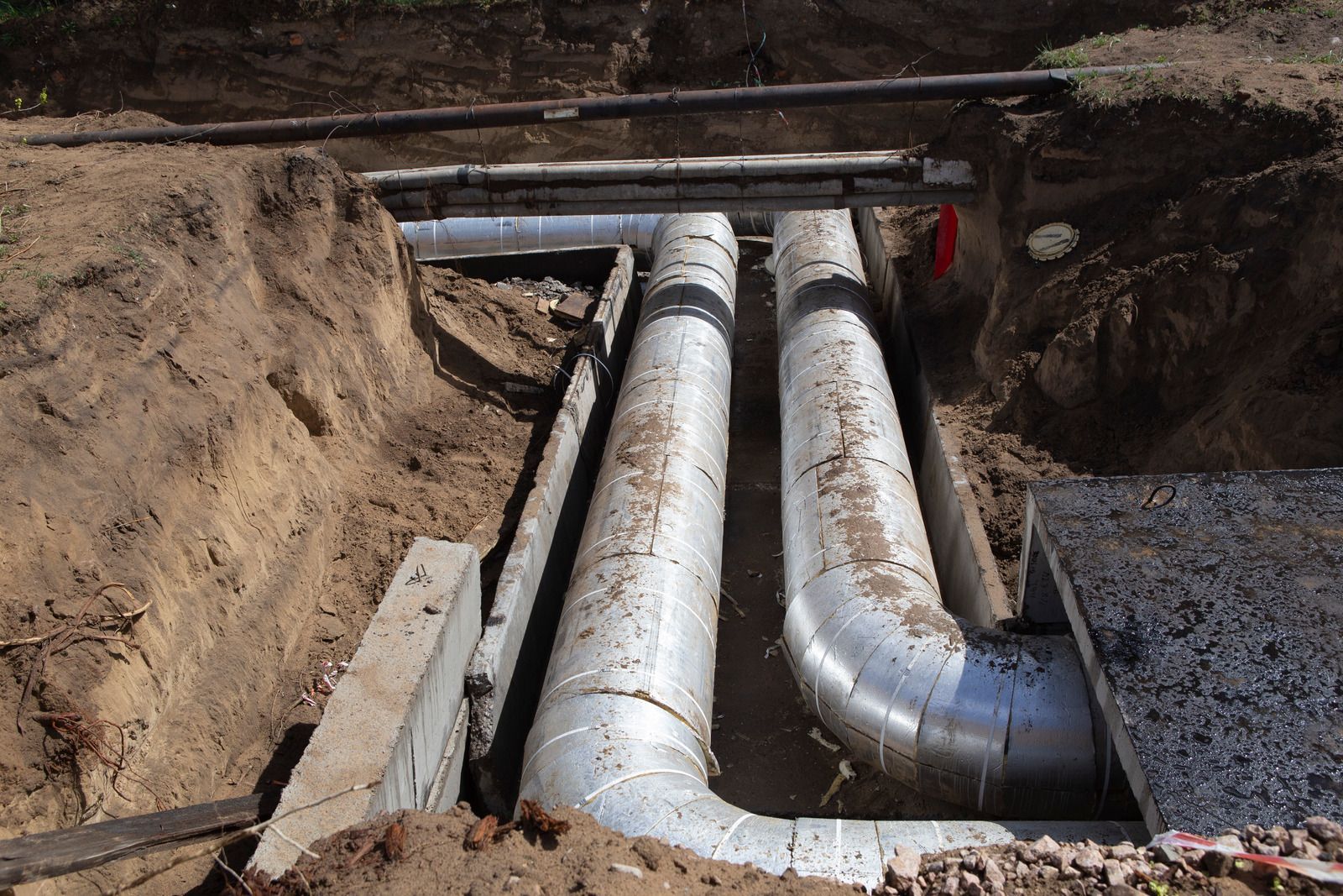 Pipes in a trench, insulated and curving, running underground.