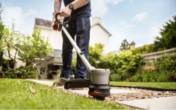 A man is using a HHT36BXB lawn trimmer to cut the grass  — Terrace Mowers in Raymond Terrace, NSW
