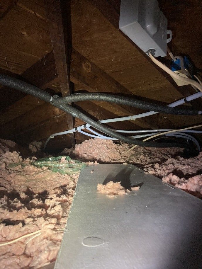 Attic view with insulation, electrical wires, and a metal plate.