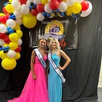 Two women in dresses are posing for a picture in front of balloons.
