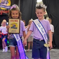 A boy and a girl are holding hands while wearing sashes and crowns.