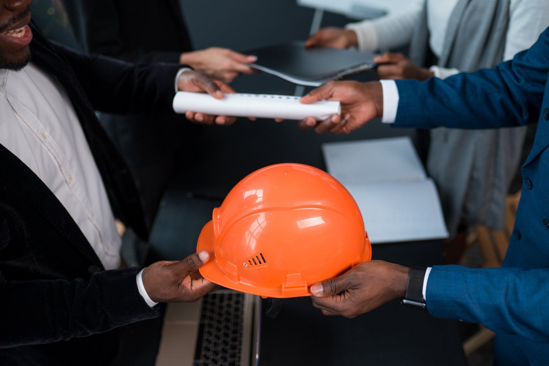 An African American man hands over a building permit and an orange construction helmet to an investor. The concept of business, construction, financing