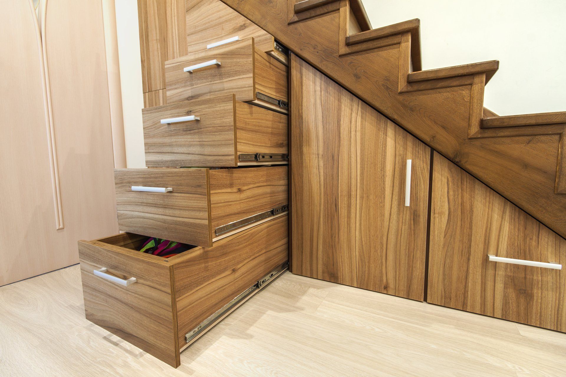 Modern architecture interior with luxury hallway with glossy wooden stairs in modern storey house. Custom built pullout cabinets on glides in slots under stairs. Use of space for storage.