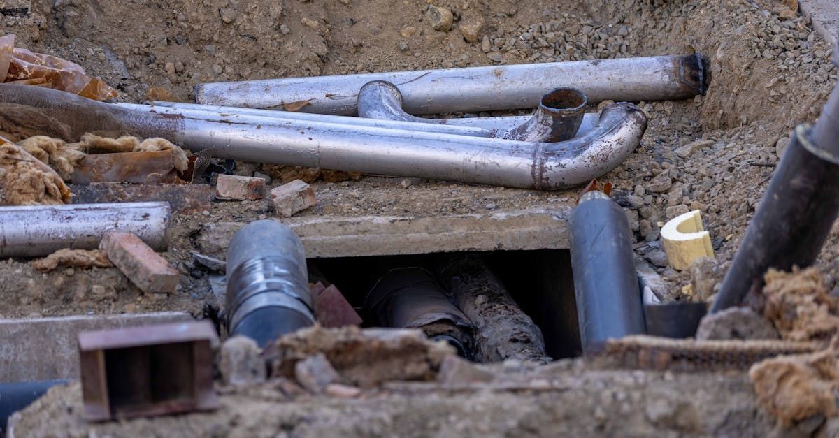 Close-up of buried pipes and broken concrete in a dirt trench