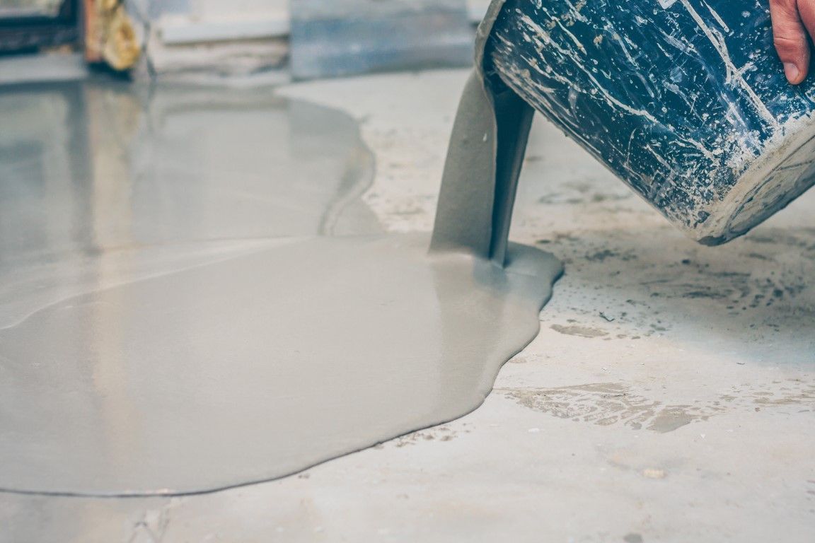 A person is pouring concrete into a hole in the floor.