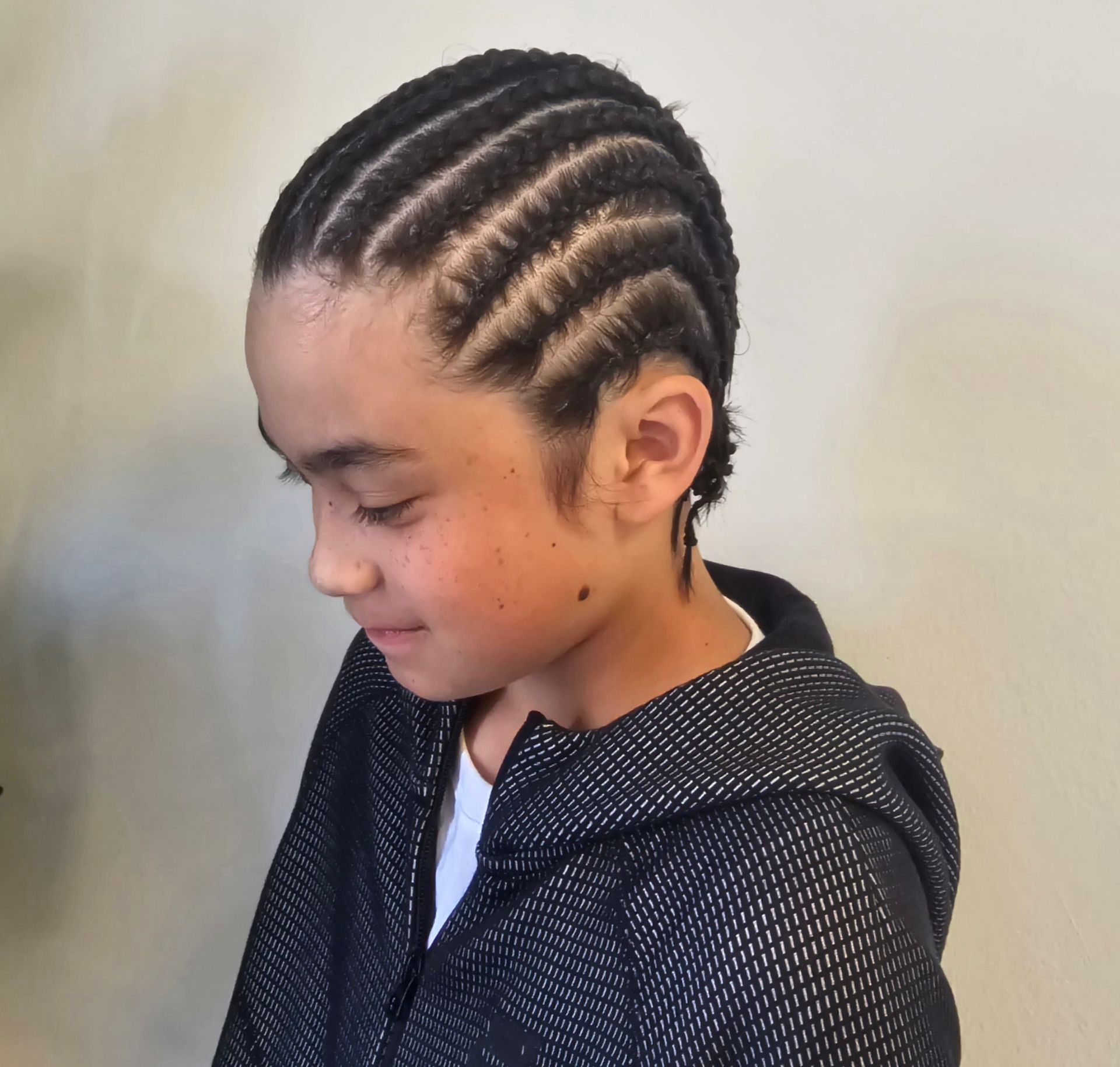 A young boy with braids in his hair is wearing a black jacket