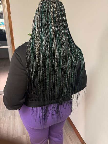 A woman with green braids and purple pants is standing in a hallway.