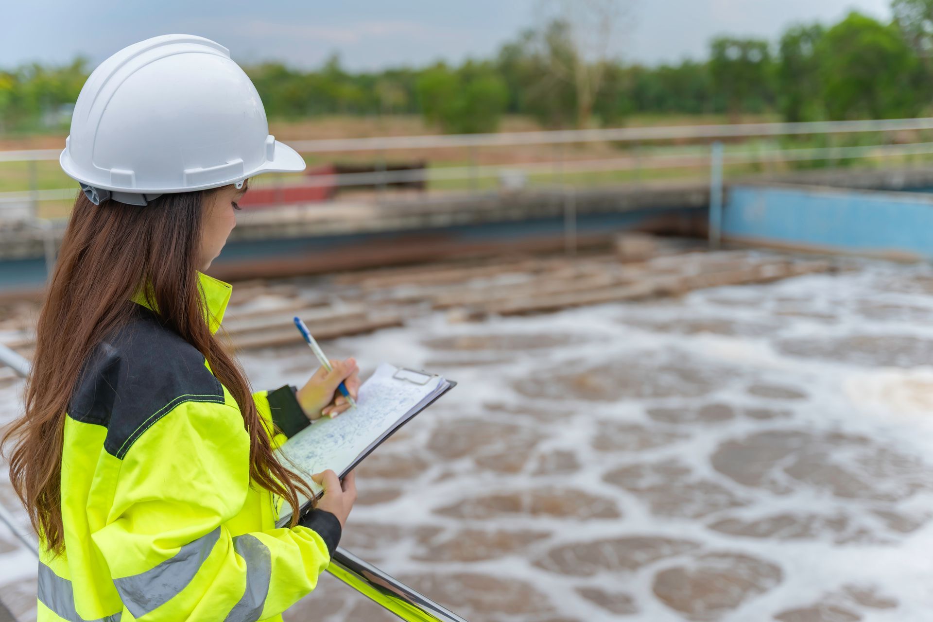 Worker in high-visibility jacket and hard hat inspecting water treatment plant with clipboard. Worker in high-visibility jacket and hard hat inspecting water treatment plant with clipboard.