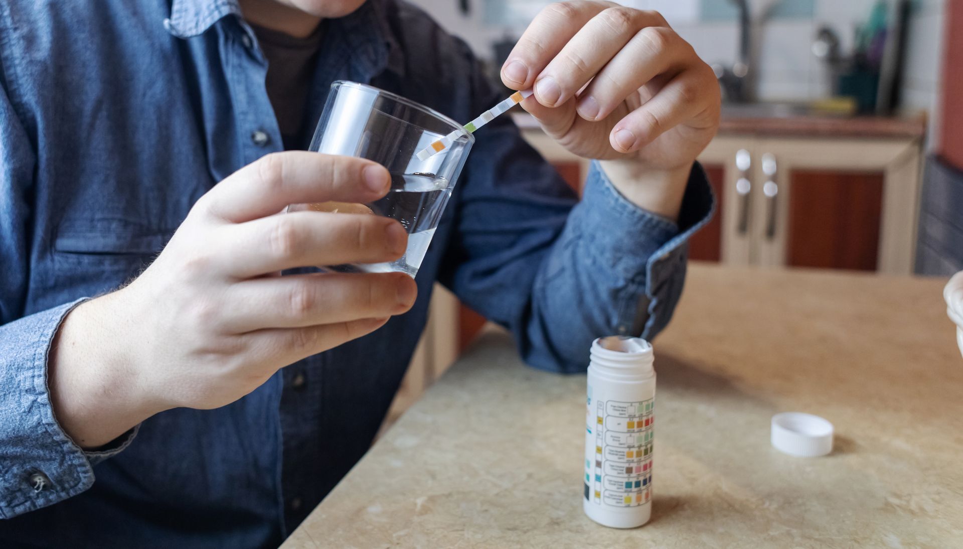 A man in the kitchen tests tap water quality with a test strip.