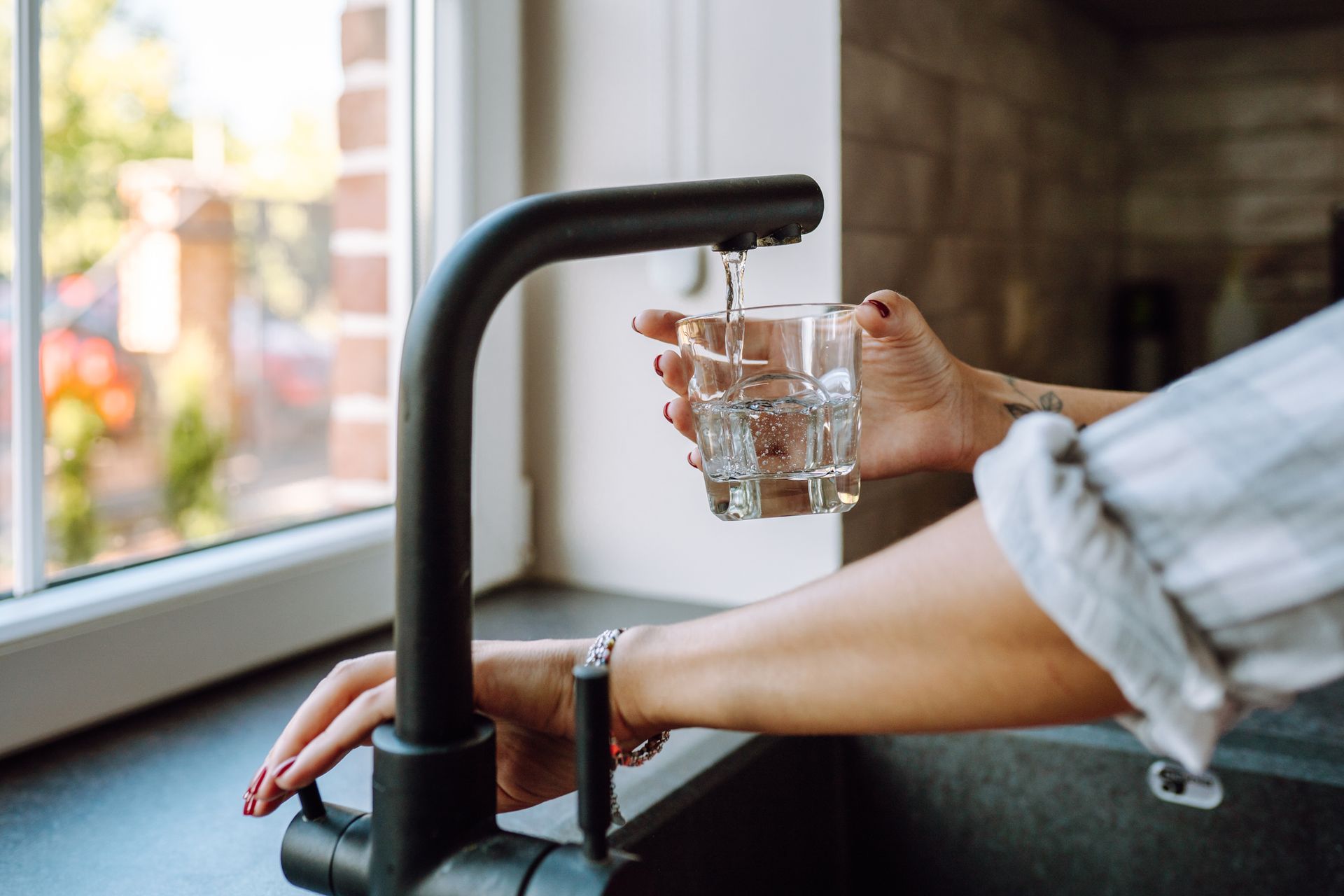 Close view of hands serving water in a glass from a black faucet inside a house. Close view of hands serving water in a glass from a black faucet inside a house.