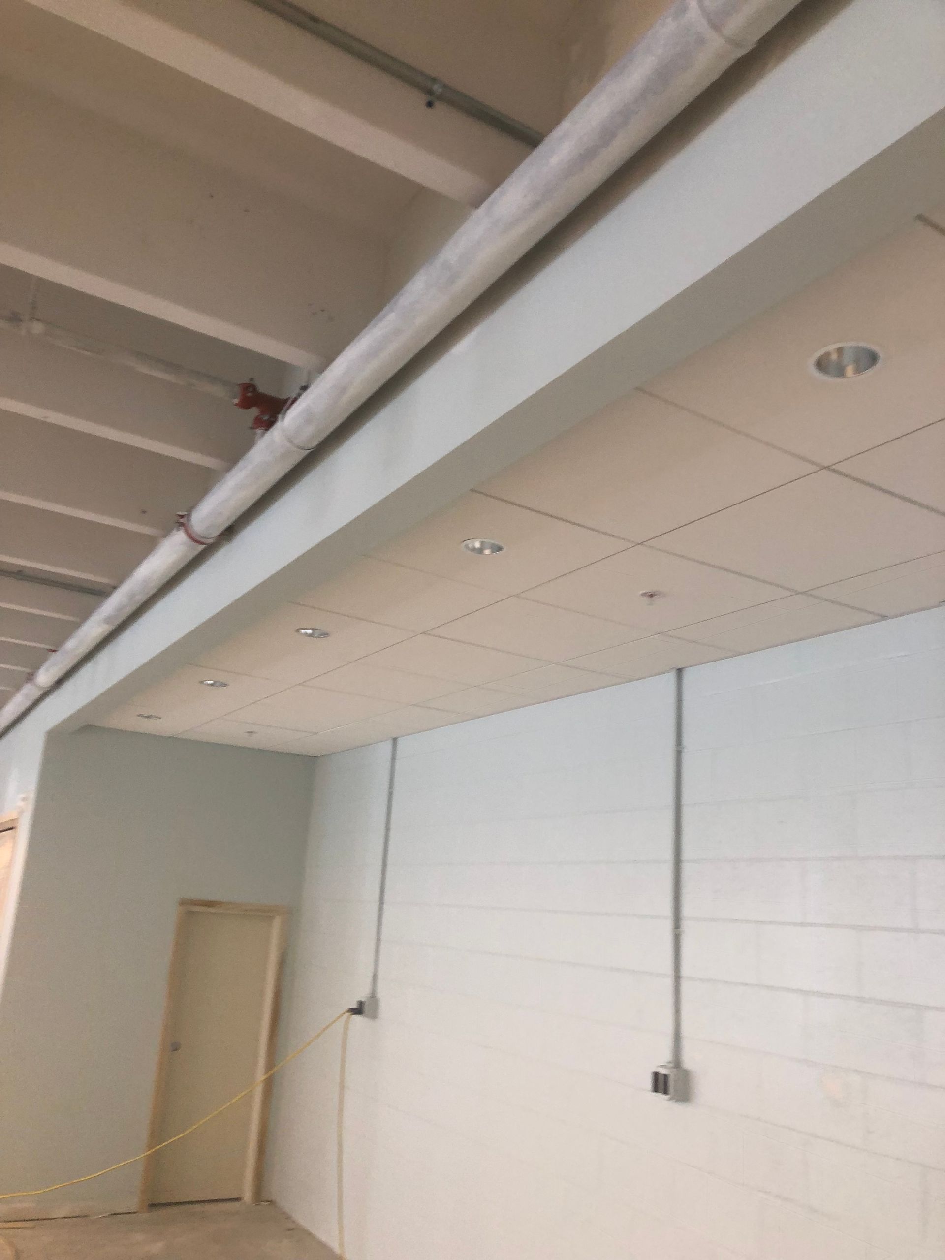 Interior view of a room with a drop ceiling, lighting, and electrical conduit. A door is on the left.