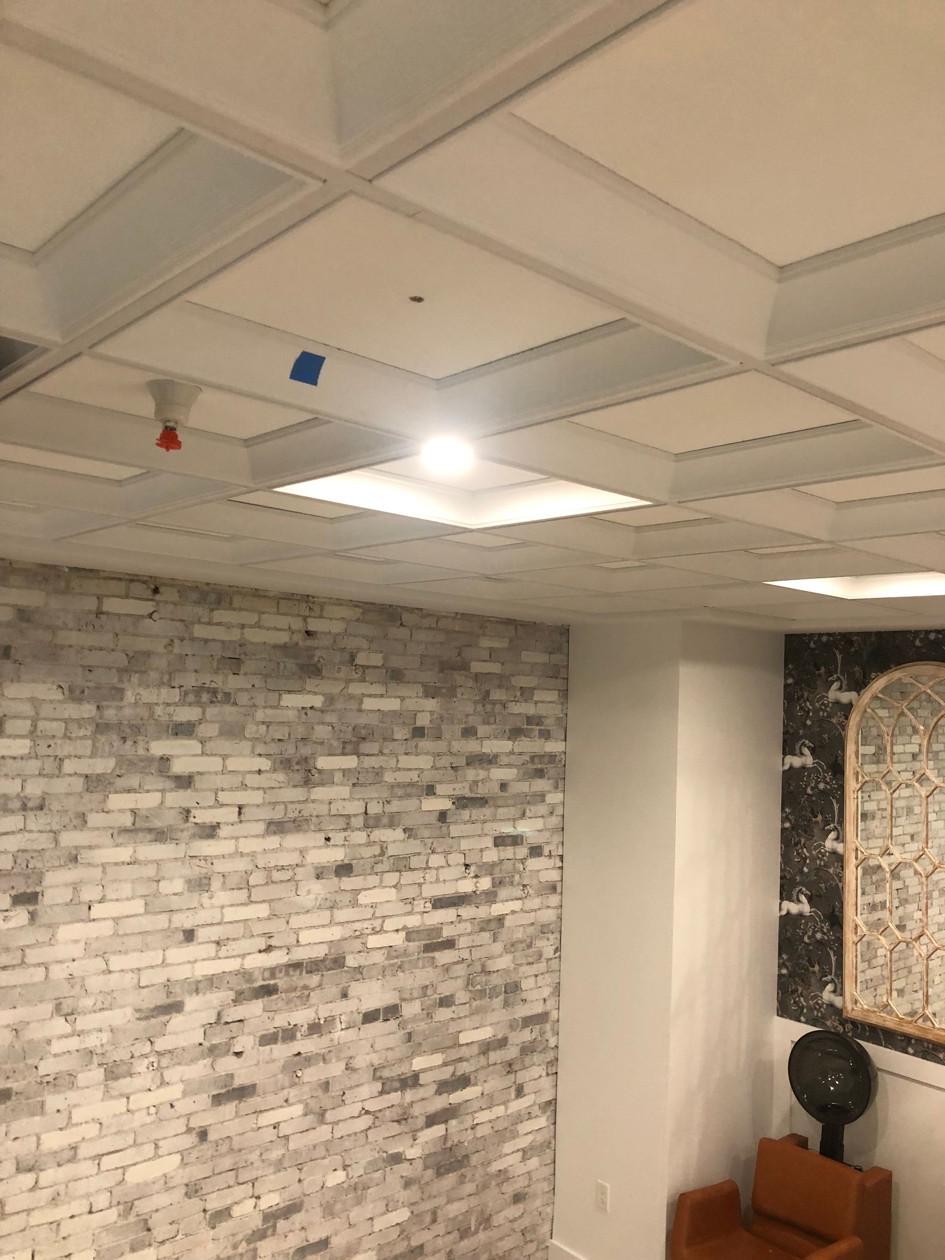 White brick wall, patterned ceiling with recessed lights, and an orange chair.