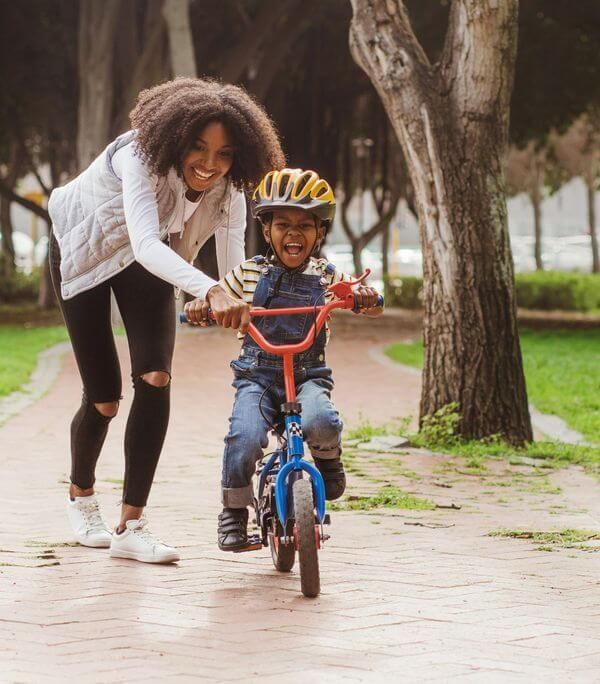 A woman is teaching a young boy how to ride a bike.