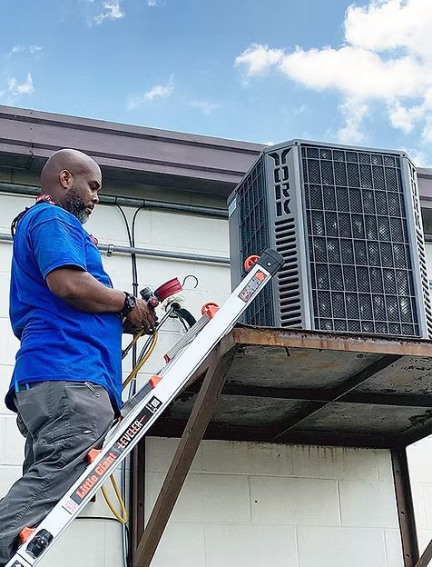 A man is standing on a ladder working on an air conditioner.