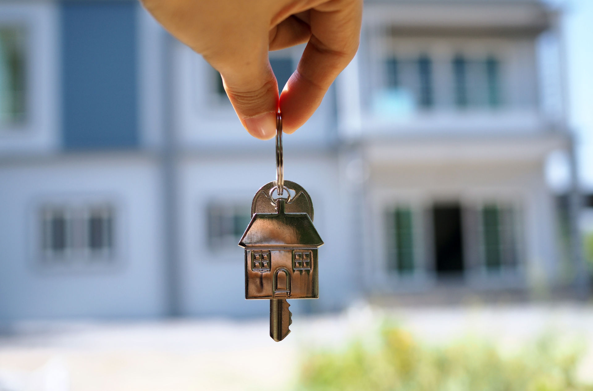 A person is holding a house key in front of a house.