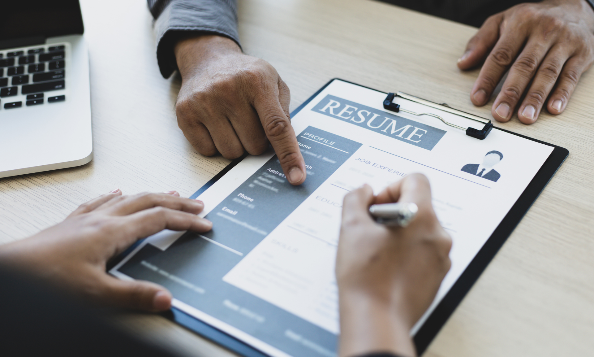 A man and a woman are looking at a resume on a clipboard.