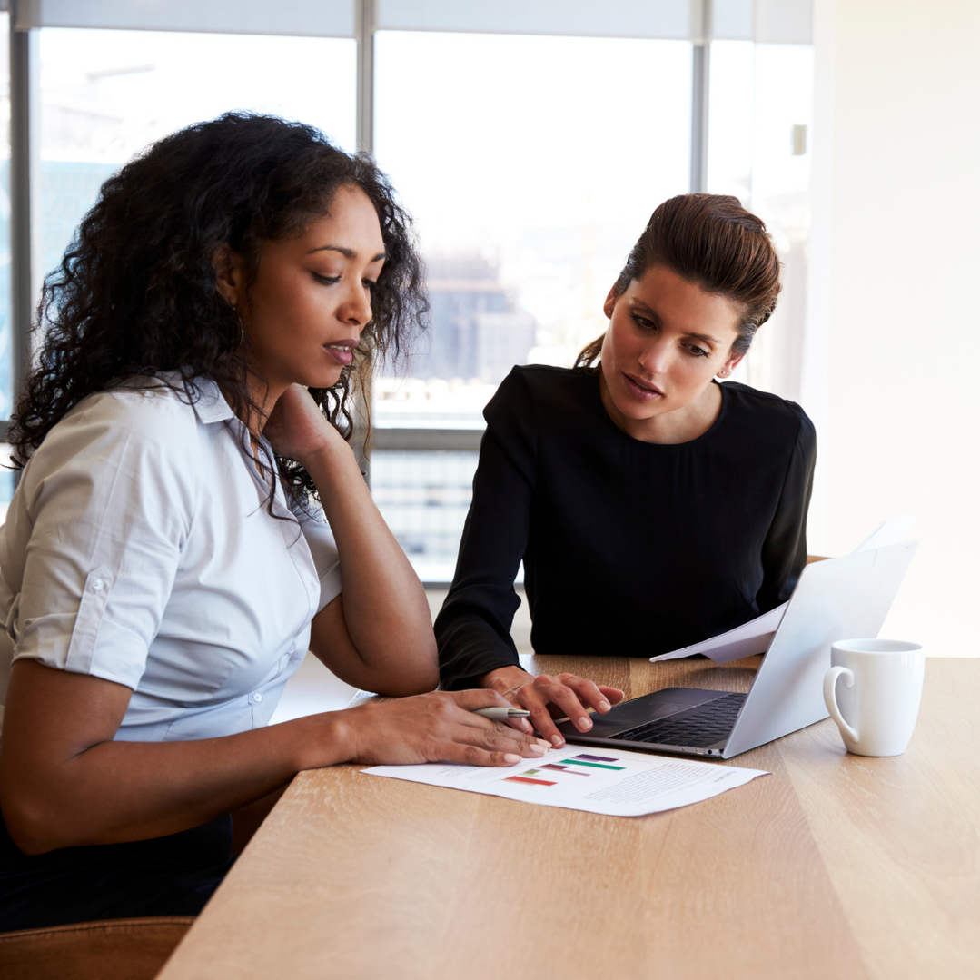 Two women are sitting at a table looking at a laptop