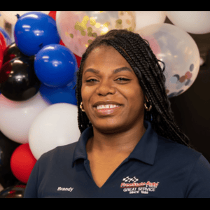 Woman with braids smiling in front of balloons, wearing a dark blue polo shirt that says