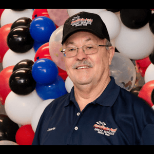 Man wearing a cap and polo shirt smiles in front of red, white, blue, and black balloons.