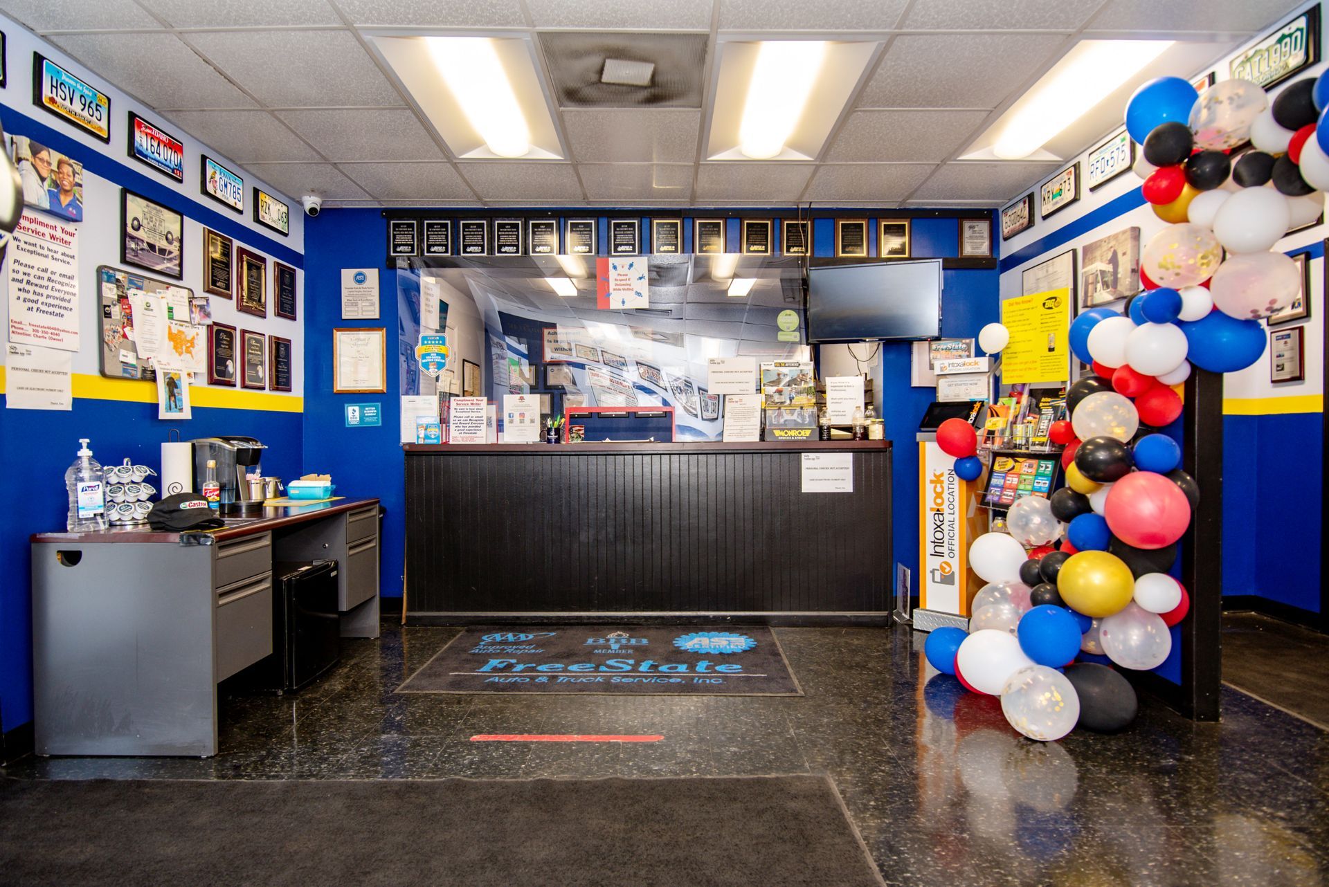 Reception area of an auto shop, featuring a counter, desk, awards, and balloons; blue and black color scheme | Freestate Auto & Truck Service